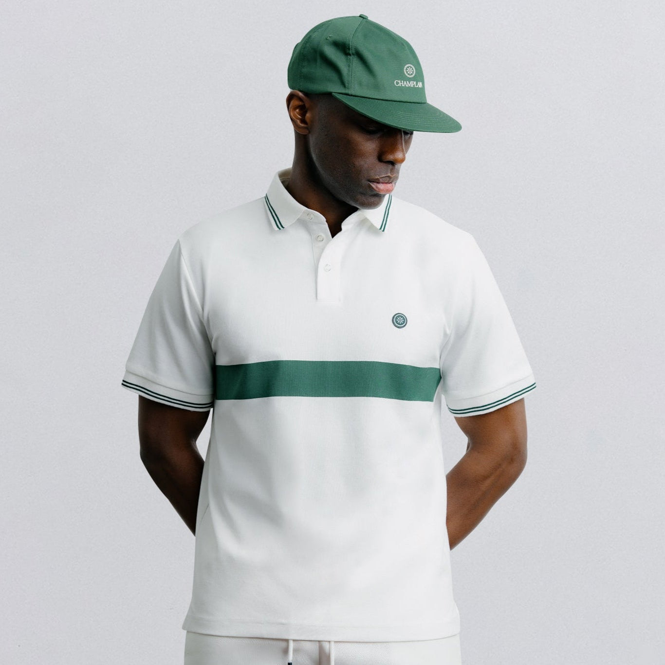 Man wearing a white polo shirt with green accents and matching shorts on a light gray background