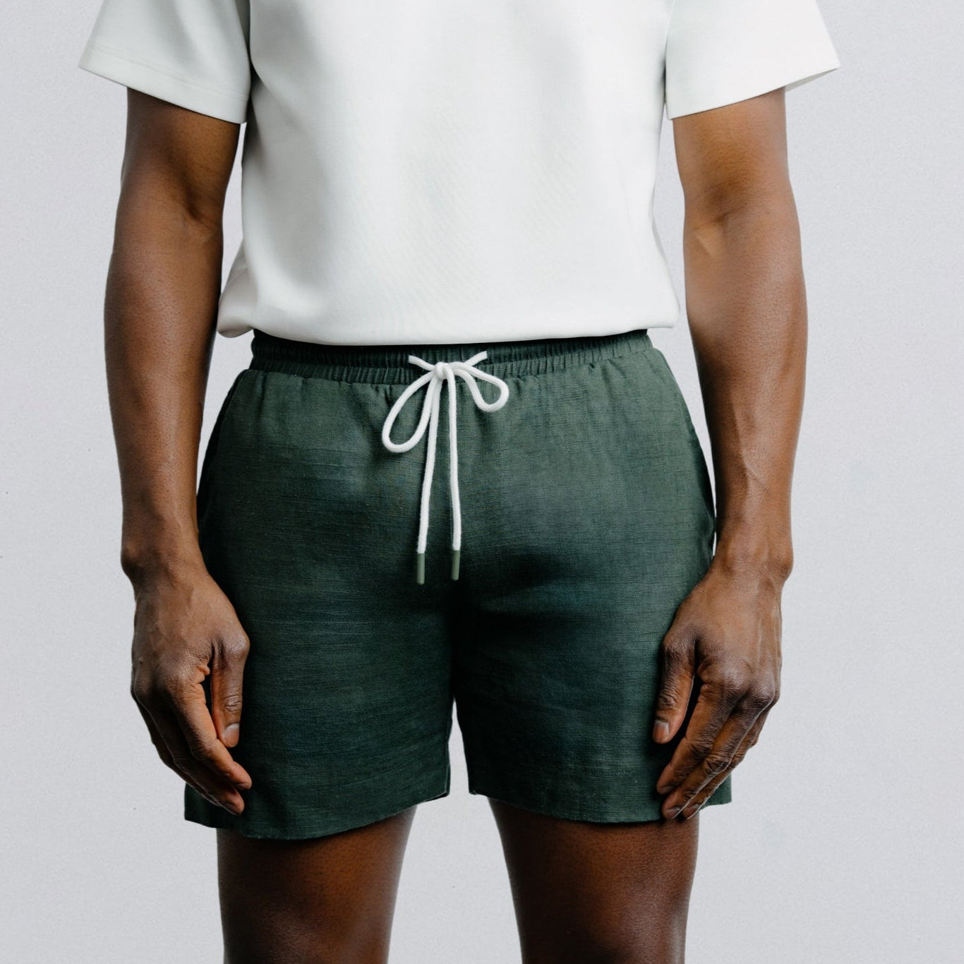 Person wearing a white t-shirt and green shorts with a white drawstring on a plain background