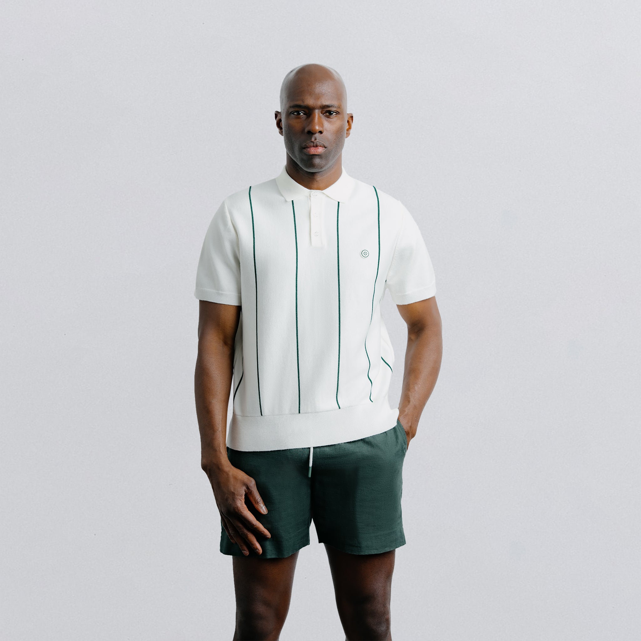 Man wearing a white polo shirt with green accents and green shorts on a light gray background