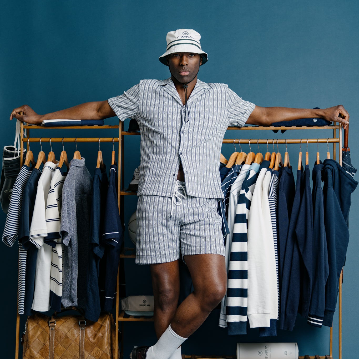 Man in a striped outfit standing next to a clothing rack against a blue background