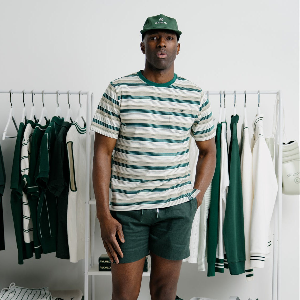 Man wearing a striped shirt and green shorts standing in a room with clothing racks.