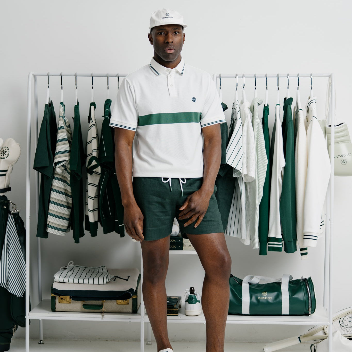 Man wearing a white polo shirt with green accents and green shorts standing in front of a clothing rack.