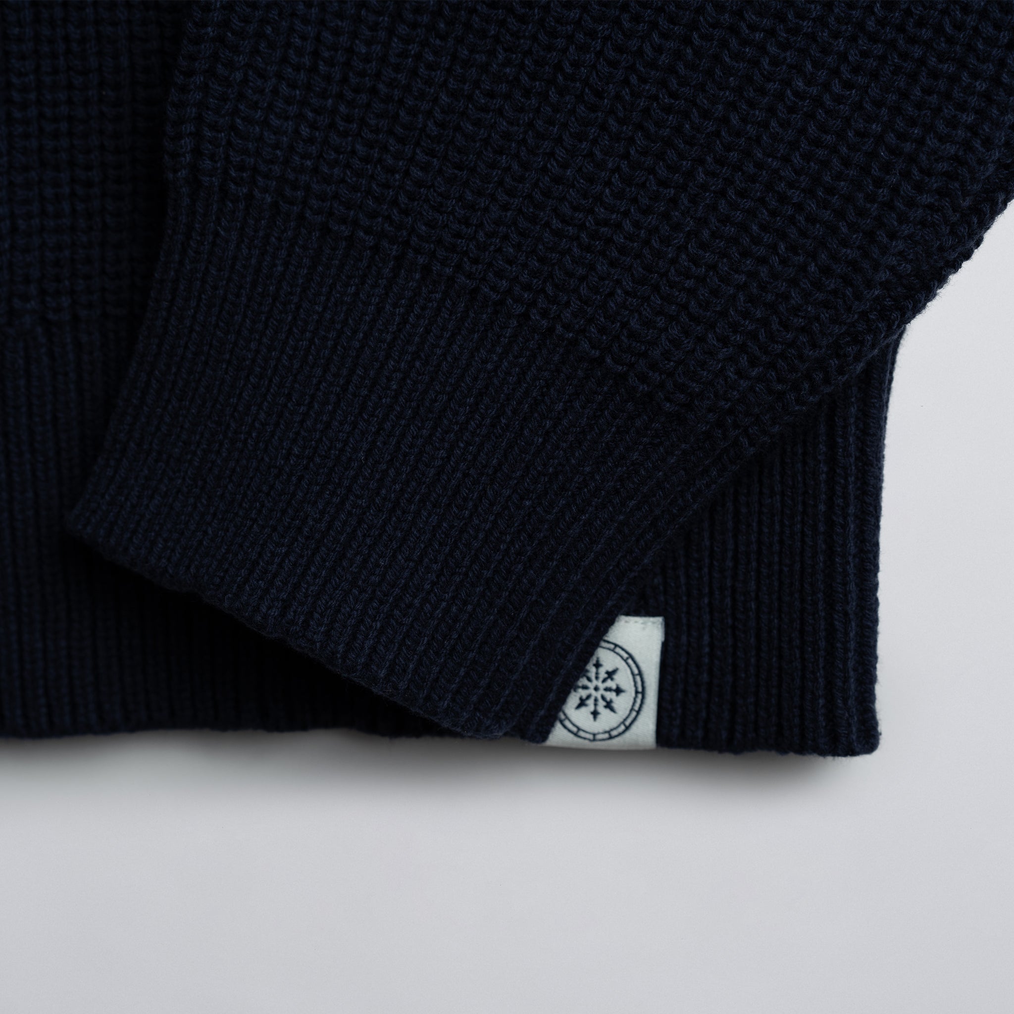 Close-up of a navy blue garment with a white label on a light gray background.