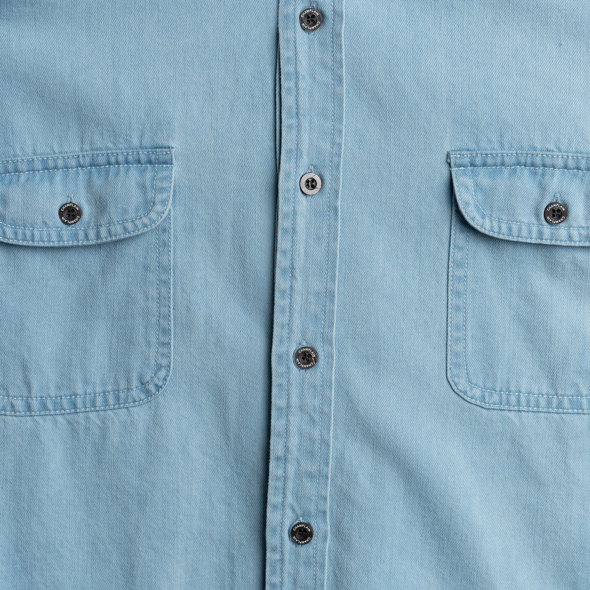 Close-up of a light blue denim shirt with buttons and pockets.