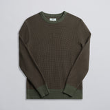 A green and brown two-tone knit sweater displayed against a neutral background