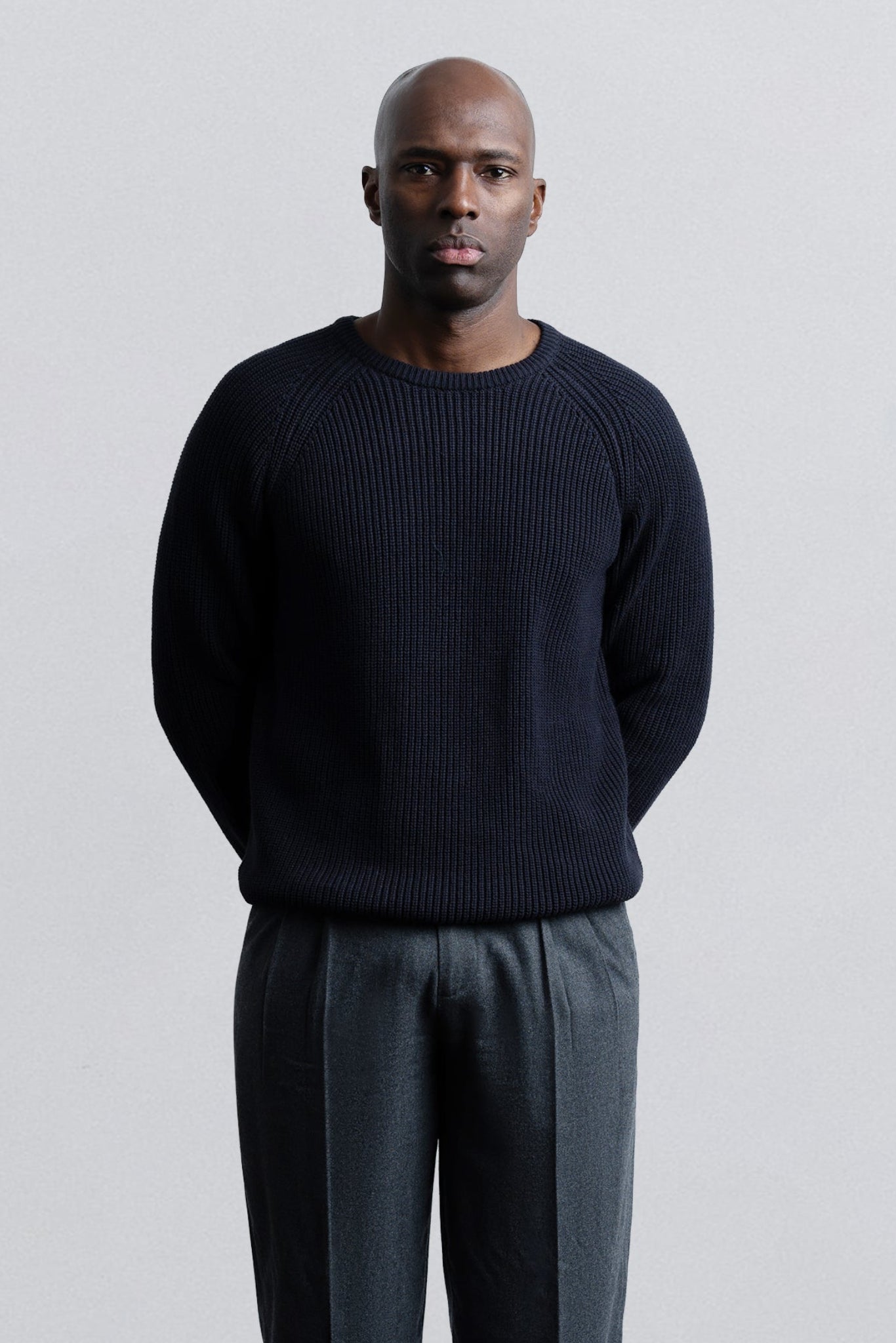 Man wearing a dark sweater and gray pants against a light gray background