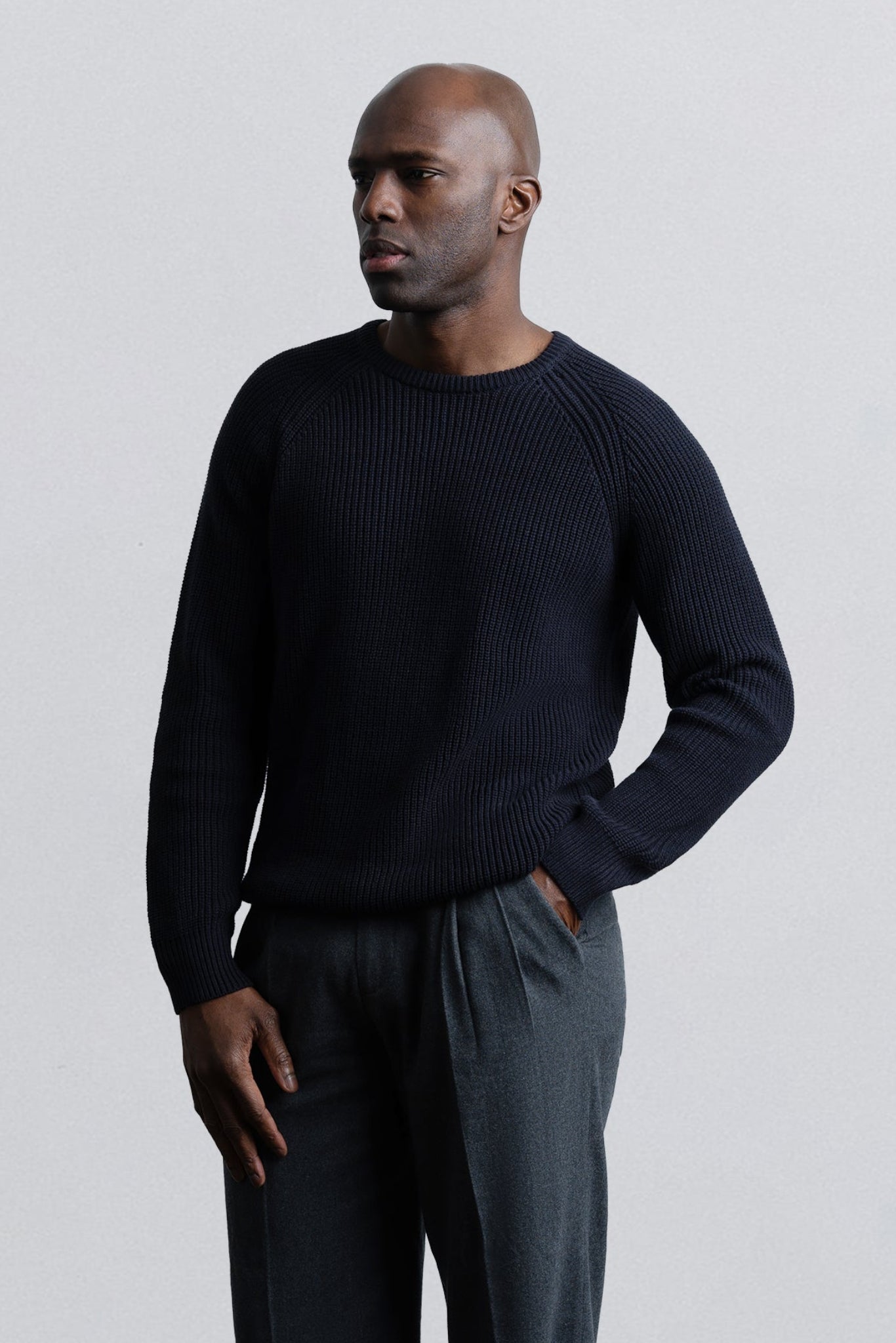 Man wearing a black sweater and gray pants against a light gray background