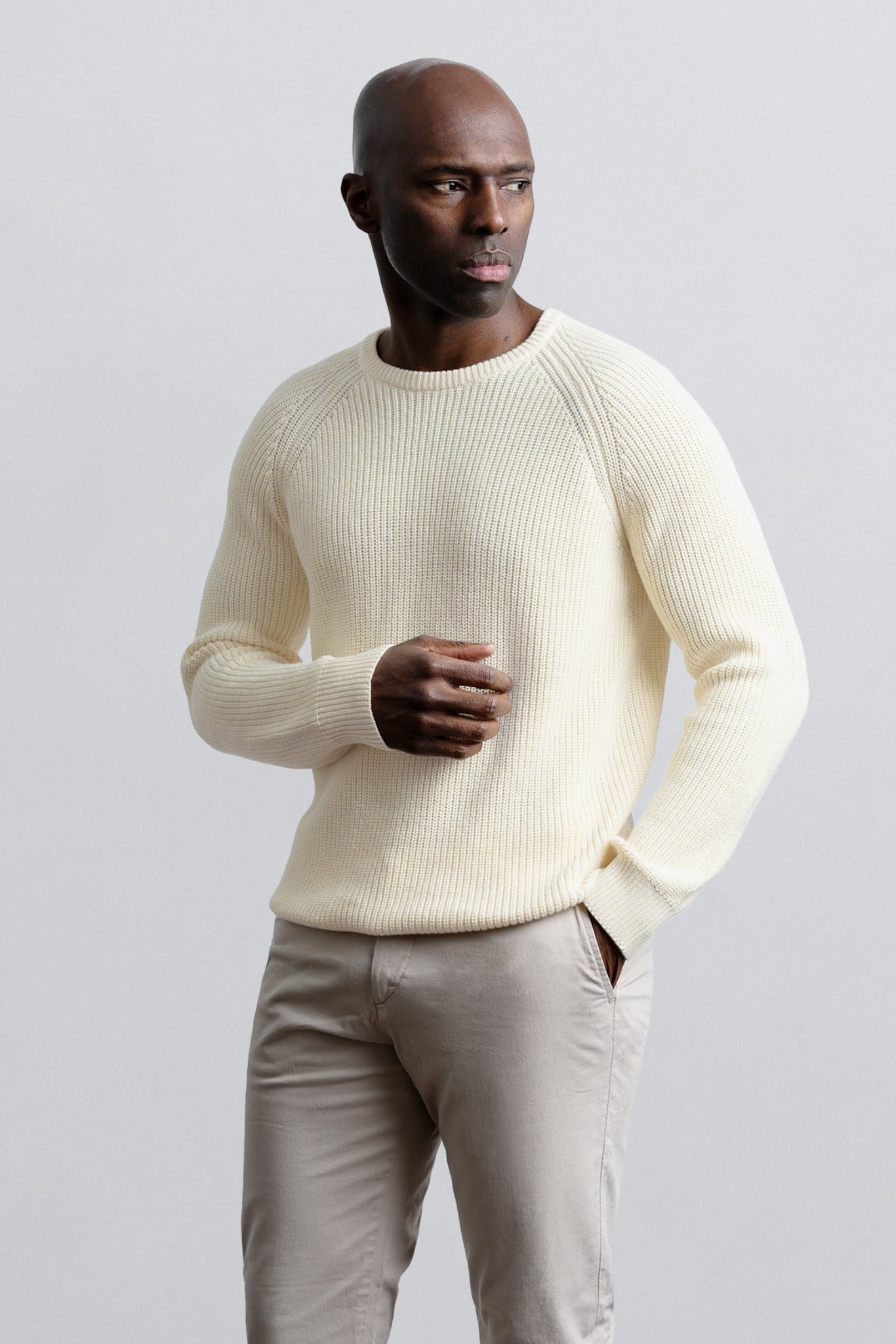 Man wearing a light-colored sweater and pants against a plain background