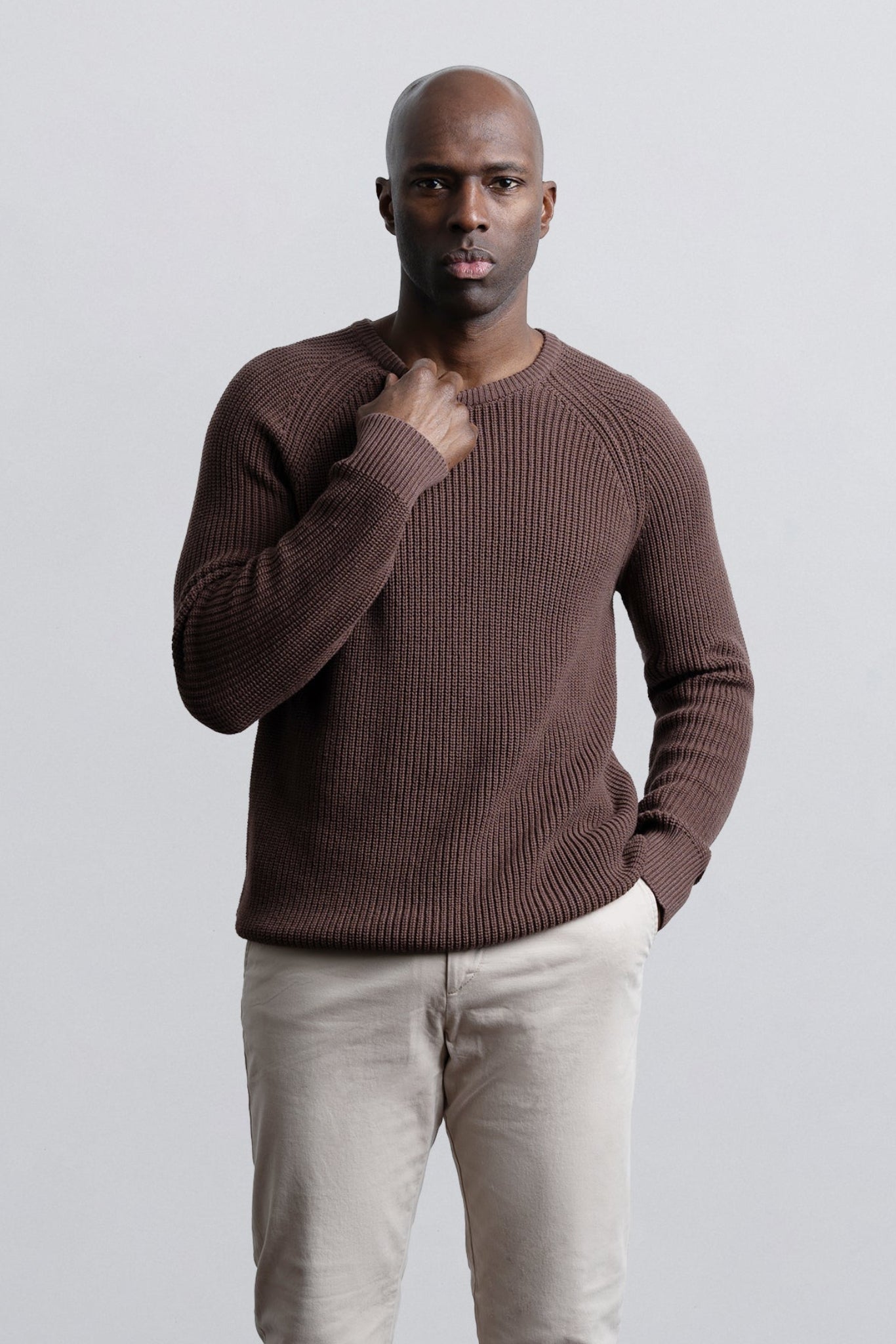 Man wearing a brown sweater and beige pants against a light gray background