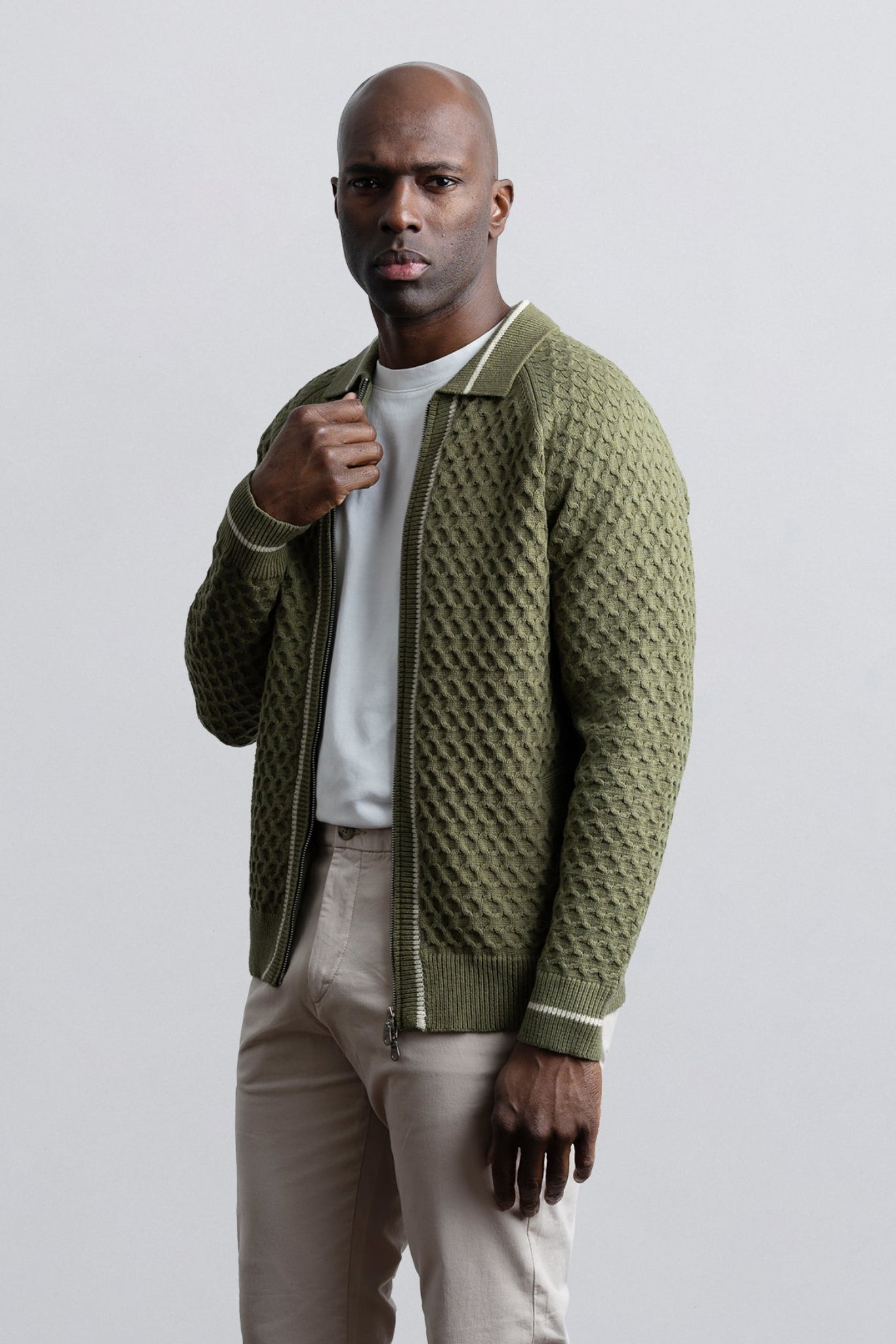 Man wearing a green textured jacket over a white shirt and beige pants on a light gray background