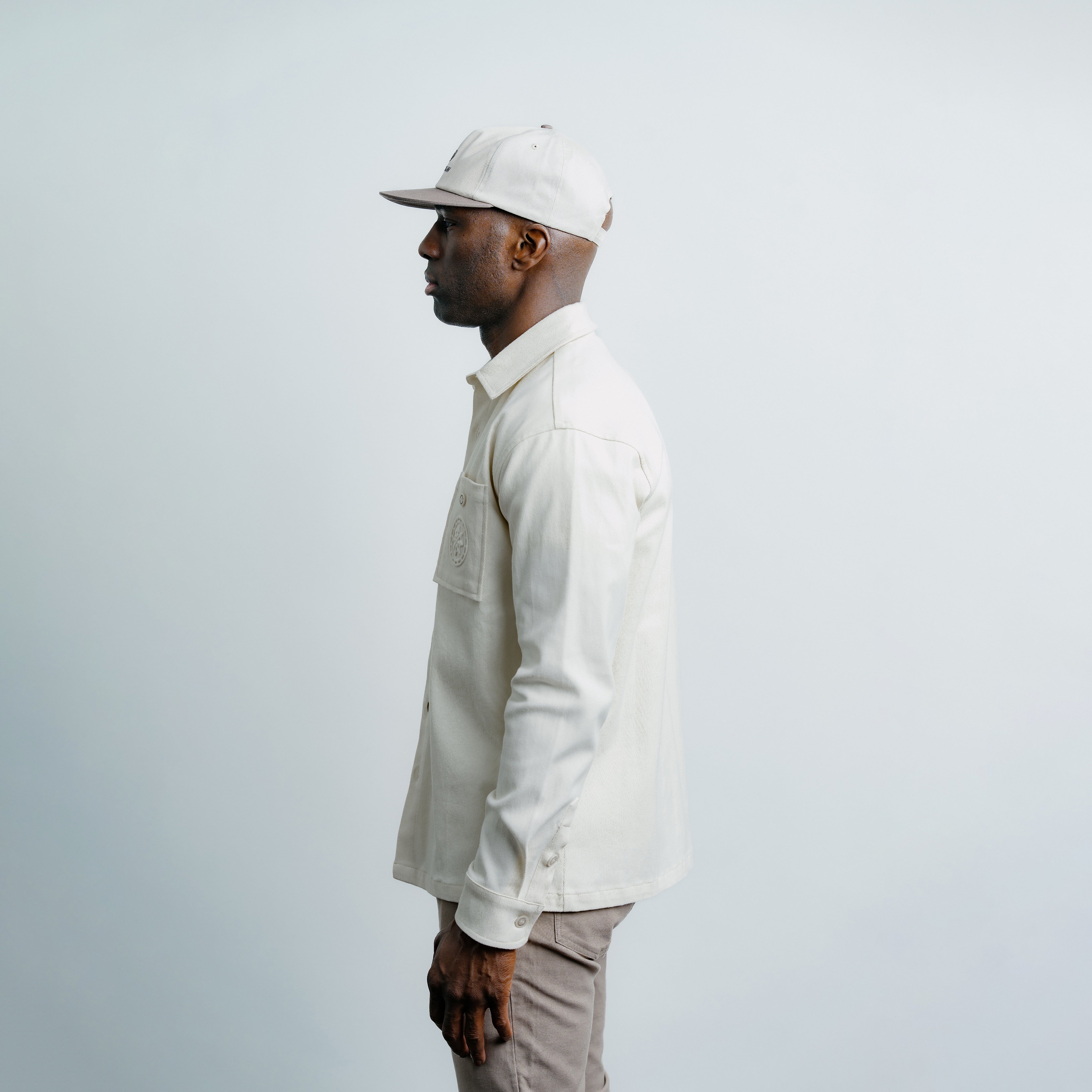 Man wearing a cream overshirt and Champlain cap against a light gray background