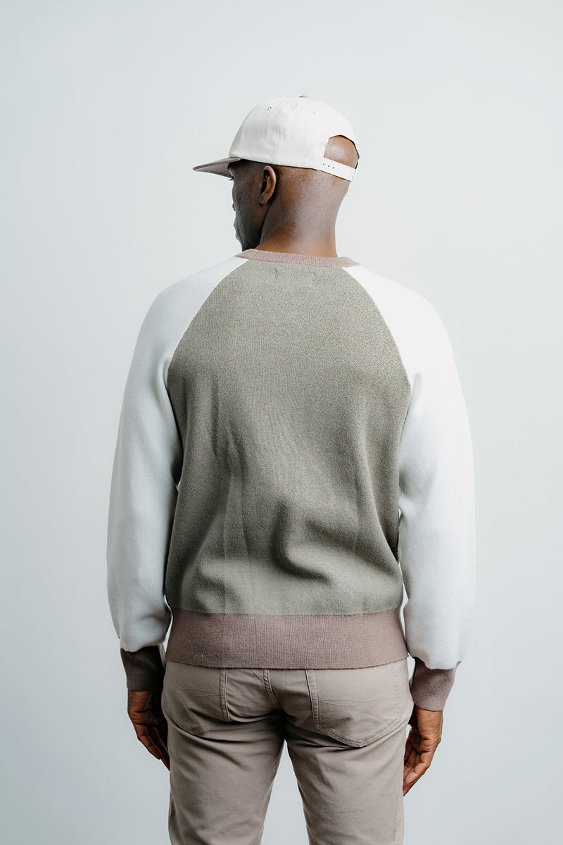 Man wearing a green and white sweater with beige pants on a plain background