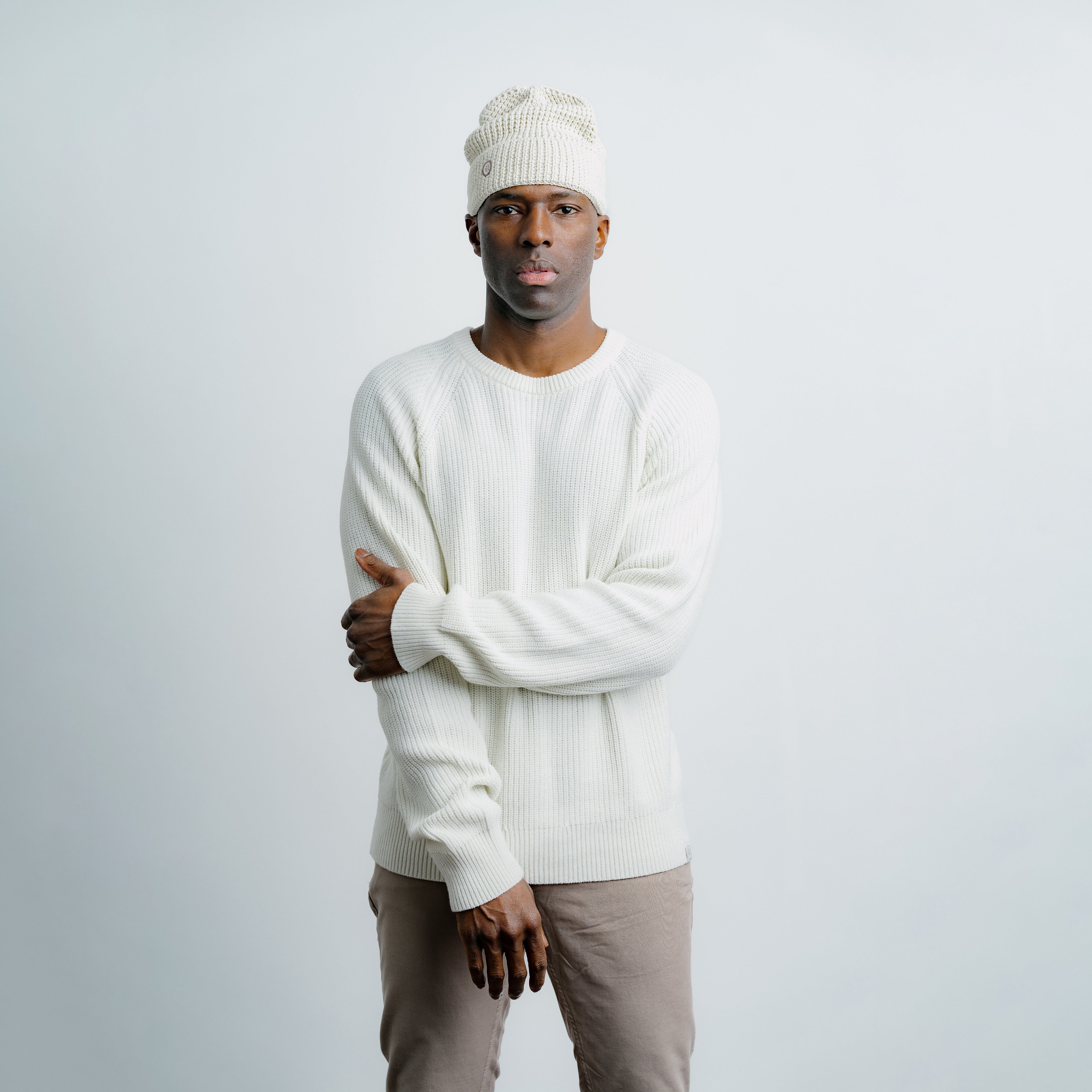 Man wearing a white sweater and knit cap against a light gray background