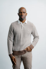 Man wearing a patterned sweater over a collared shirt with a plain background