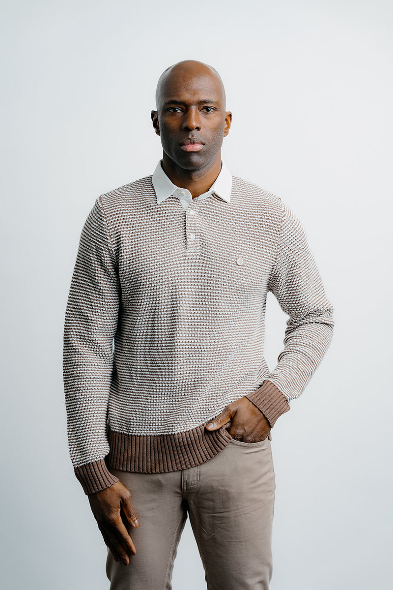 Man wearing a patterned sweater over a collared shirt with a plain background