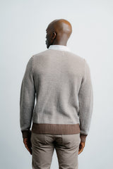 Man wearing a patterned sweater and beige pants against a plain background