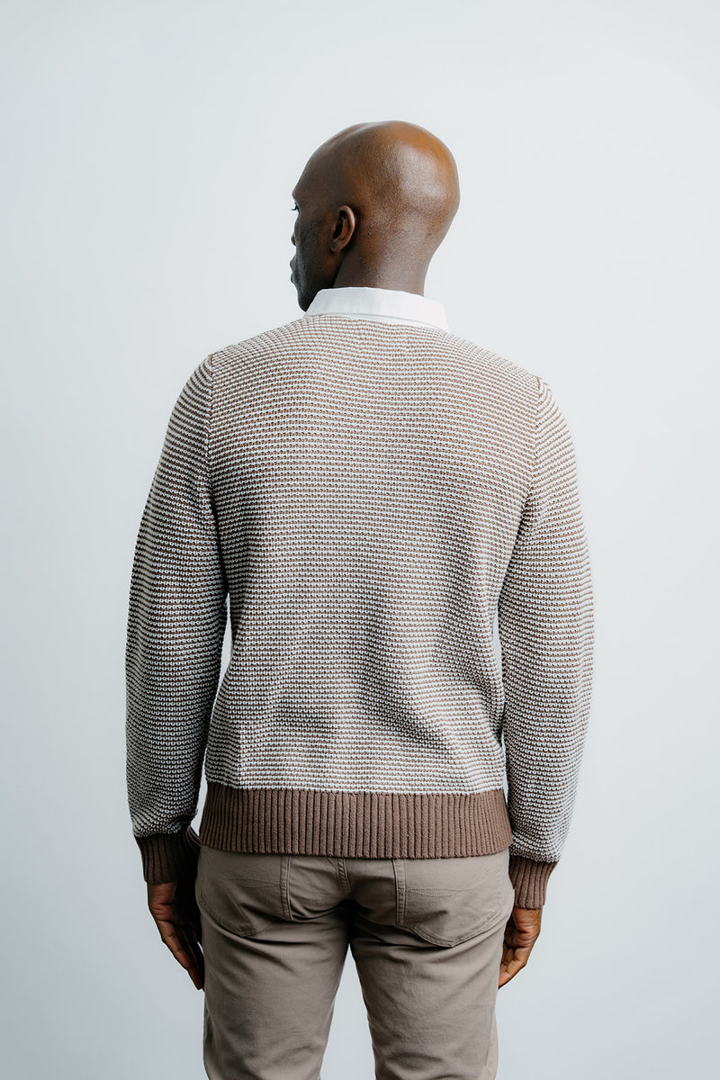 Man wearing a patterned sweater and beige pants against a plain background
