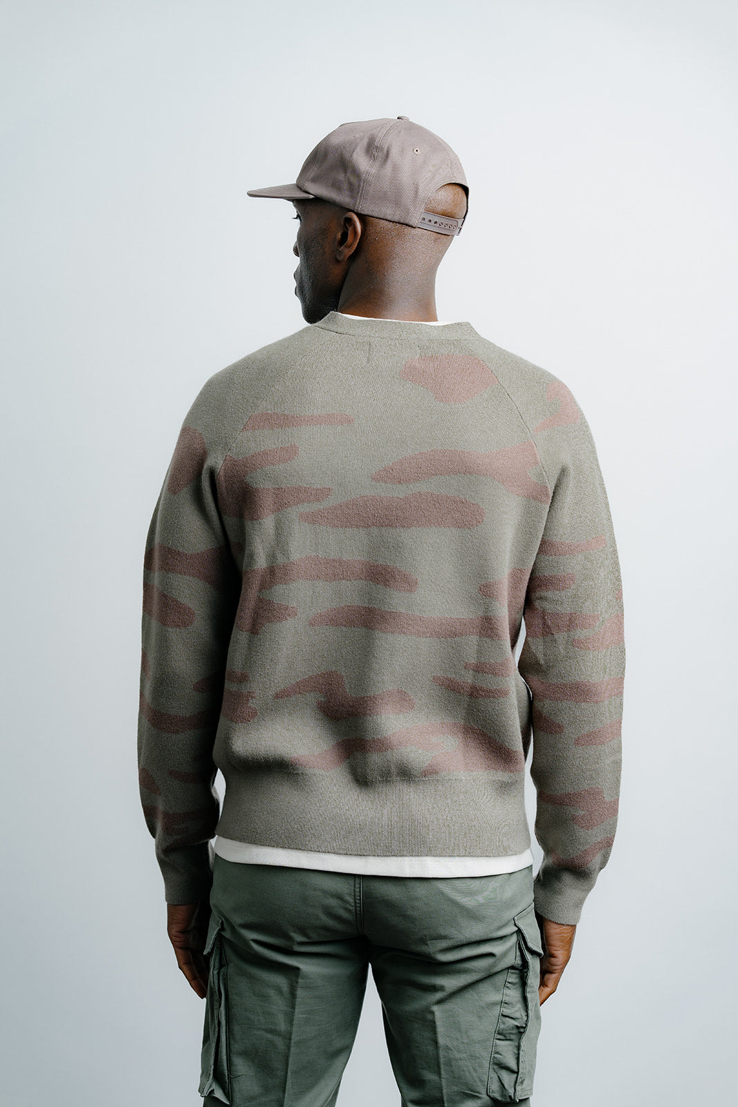 Person wearing a camouflage-patterned sweater and cap on a plain background