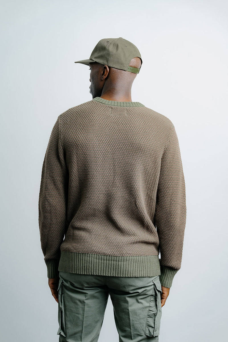 Person wearing a brown sweater and green cap with a plain background