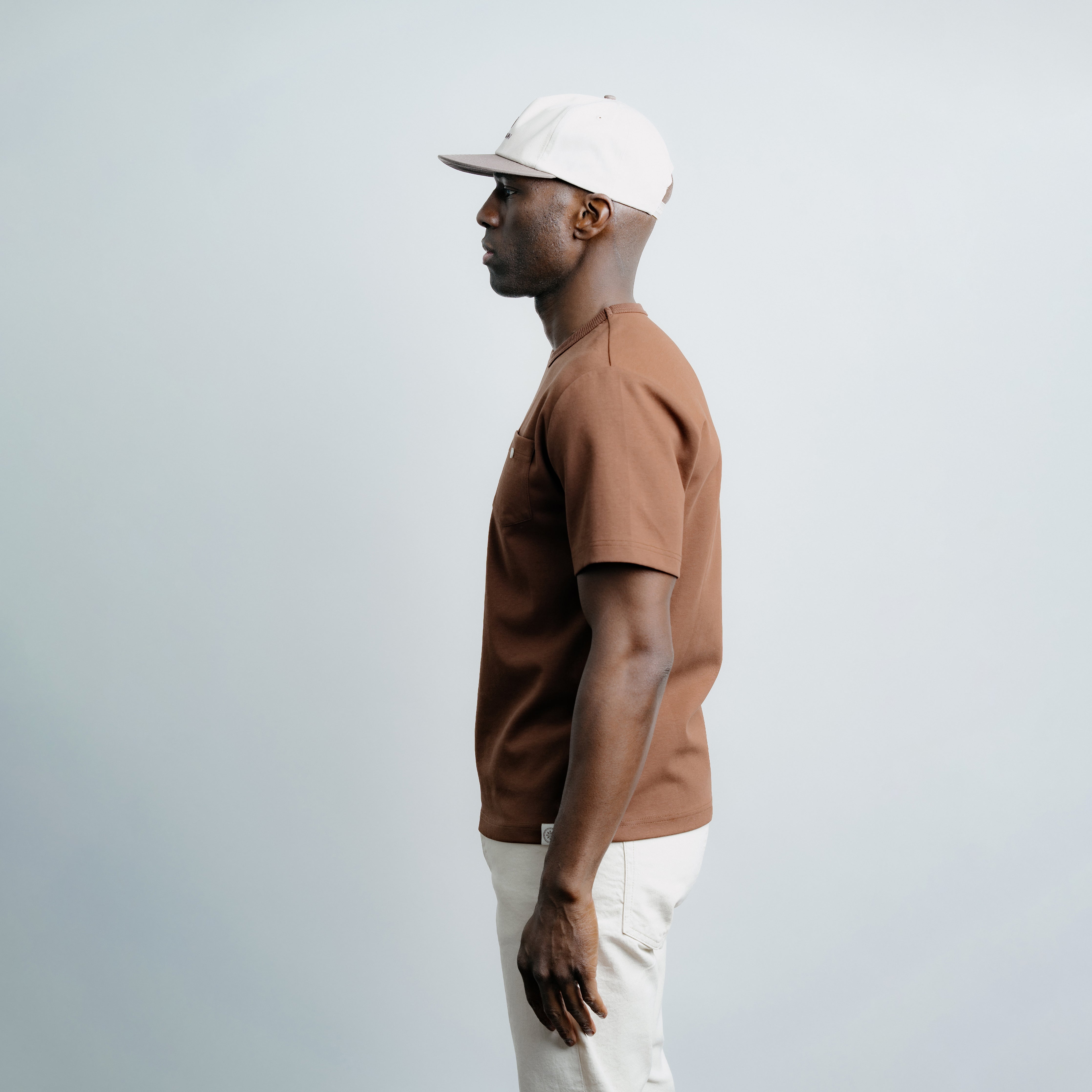 Man wearing a brown polo shirt and white cap against a light gray background
