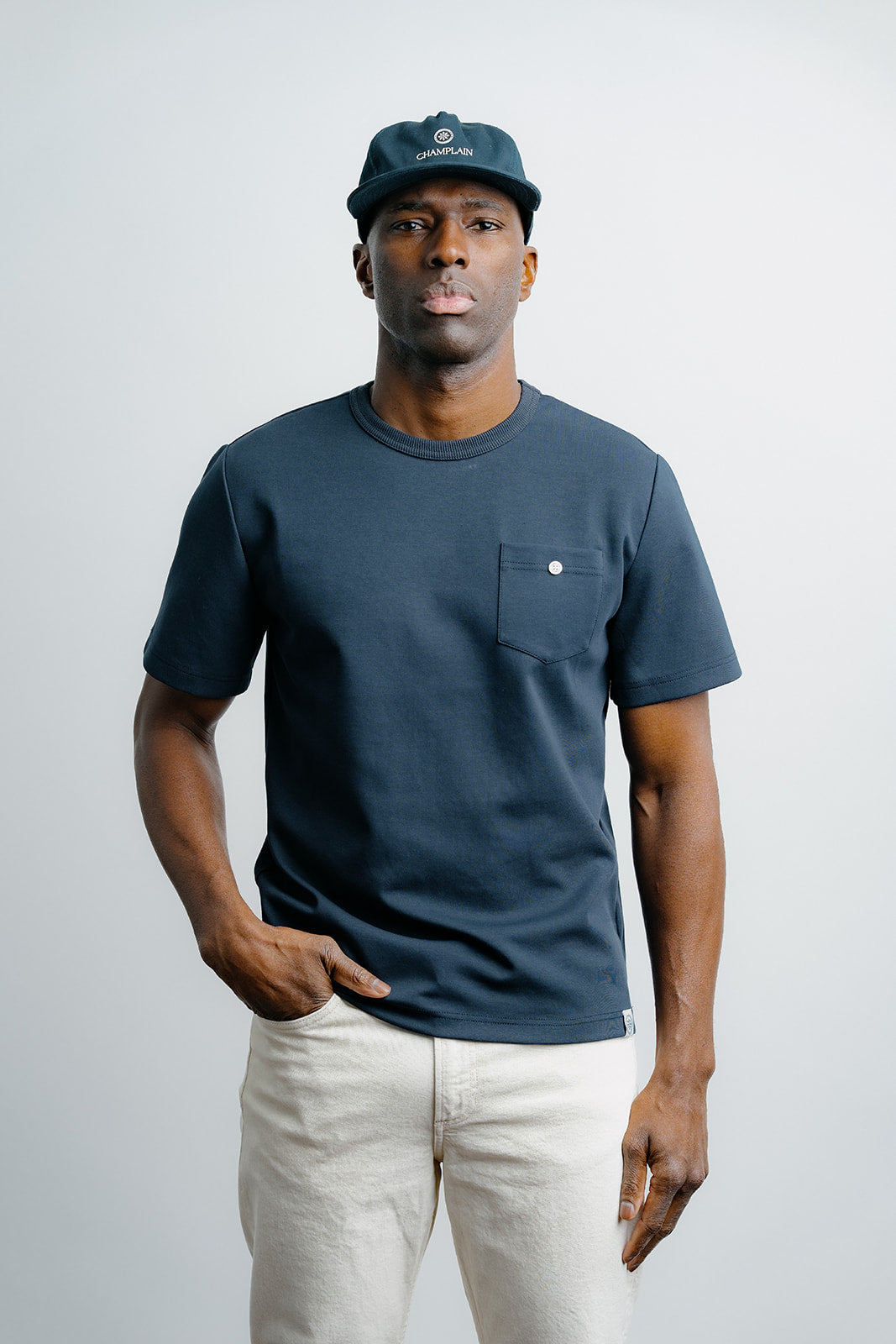 Man wearing a navy t-shirt with a pocket and a cap on a white background
