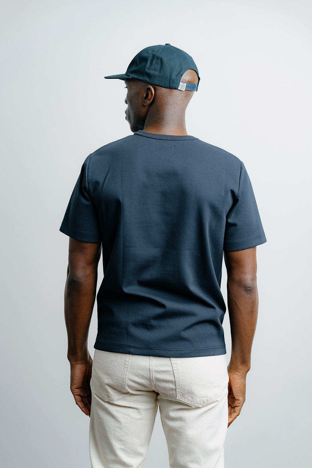 Man wearing a dark blue t-shirt and cap, standing against a plain background
