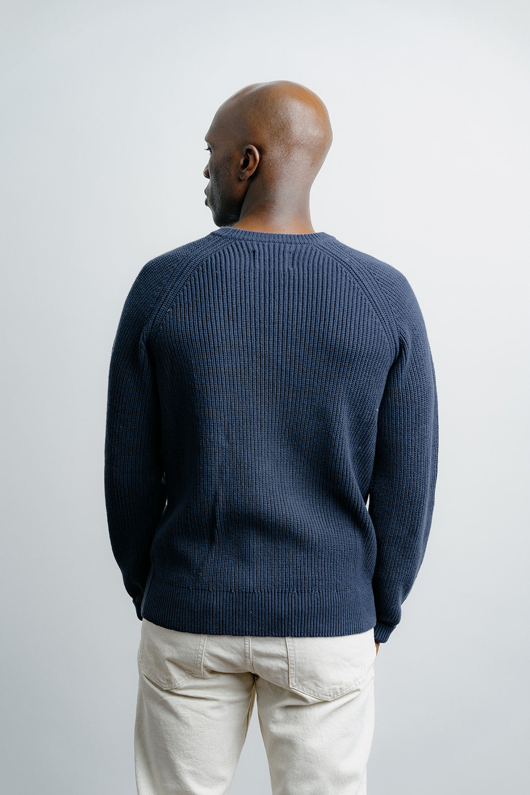 Man wearing a navy sweater and light-colored pants against a white background