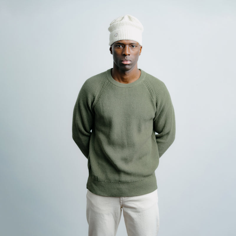 Man wearing a green sweater and white beanie against a light gray background