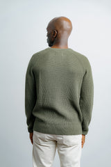 Man wearing a green sweater and beige pants against a white background