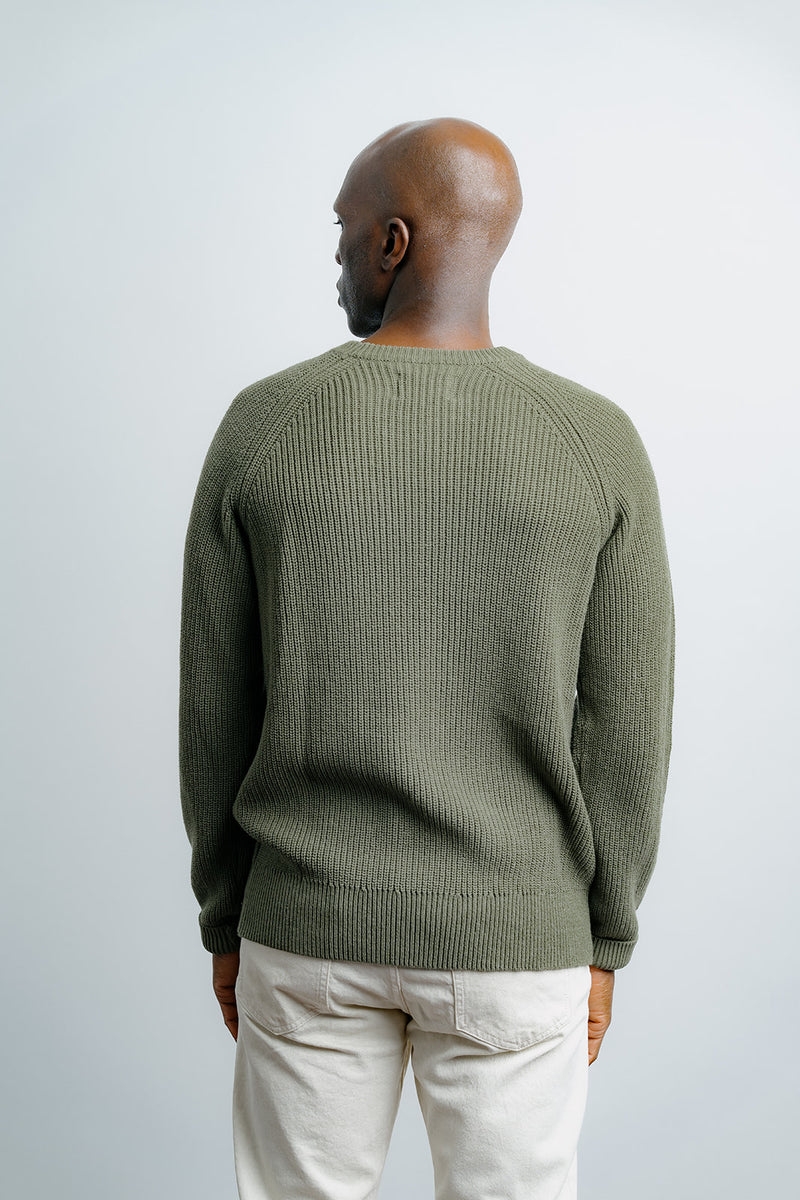Man wearing a green sweater and beige pants against a white background