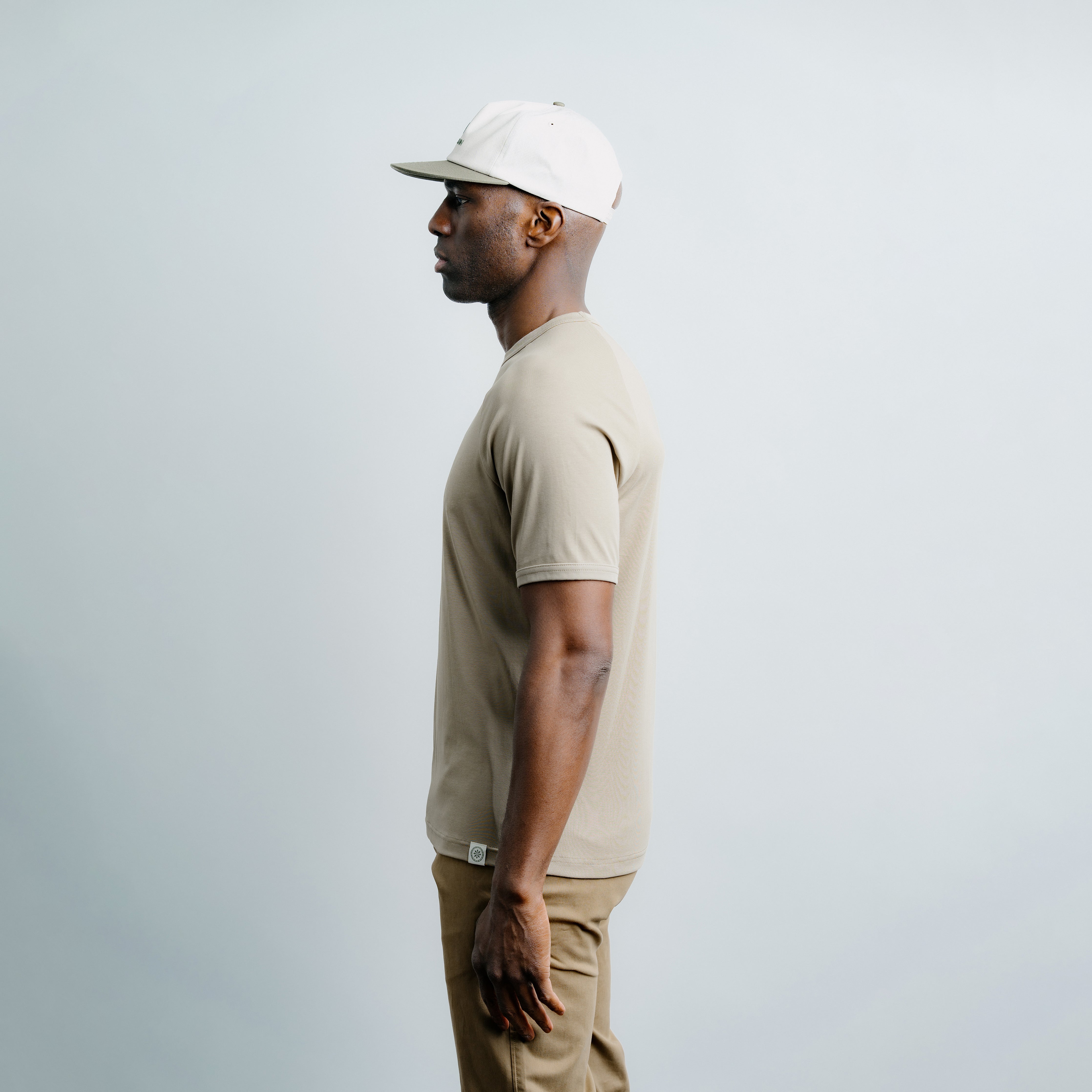 Man wearing a beige t-shirt and cap against a plain background