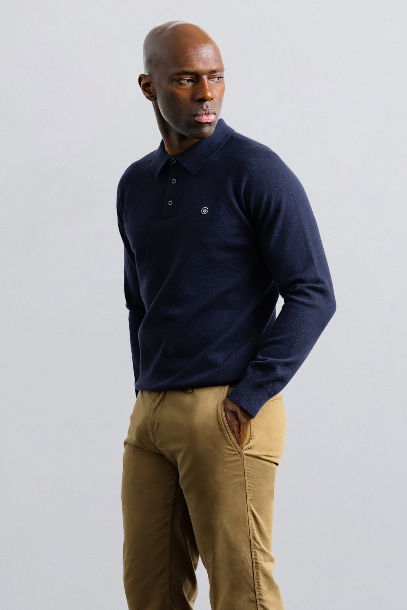 Man wearing a navy blue polo shirt and beige pants against a light gray background