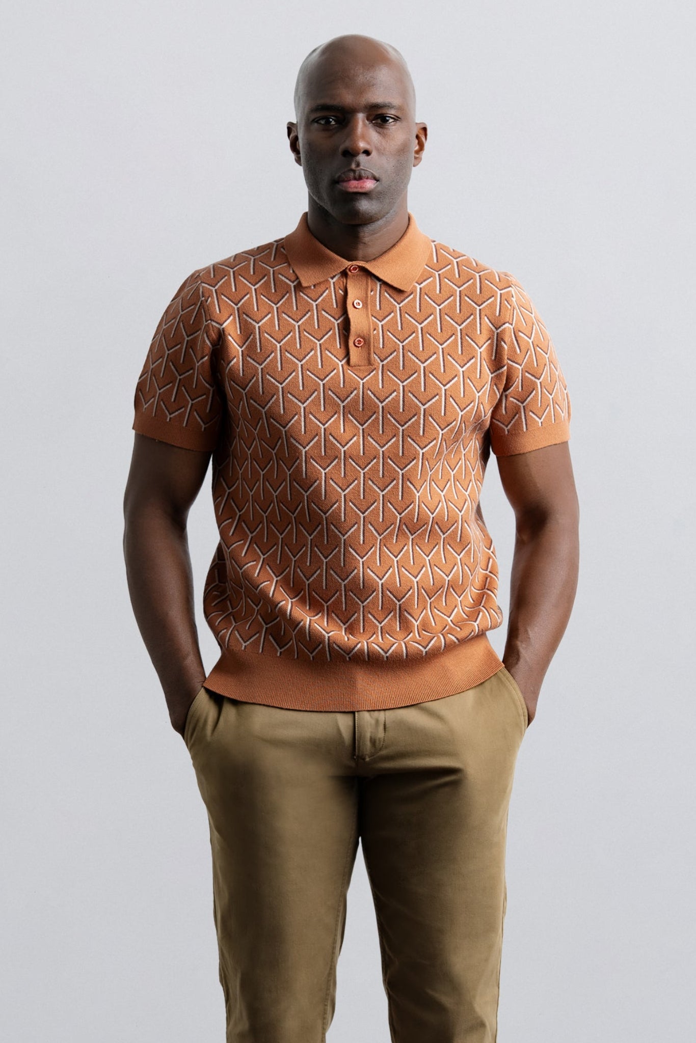 Man wearing a patterned brown shirt and beige pants against a light gray background