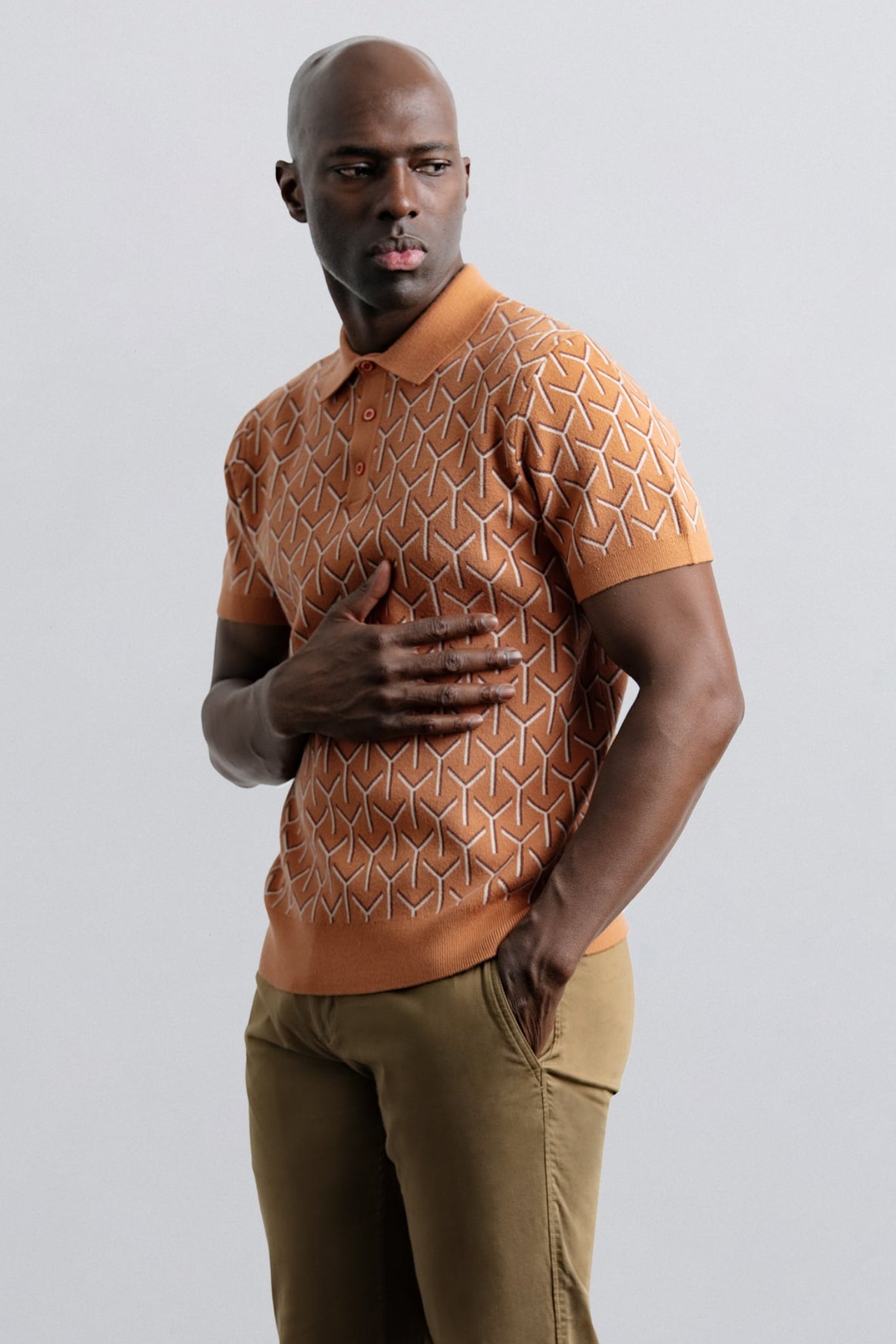Man wearing a patterned orange shirt and beige pants on a light gray background
