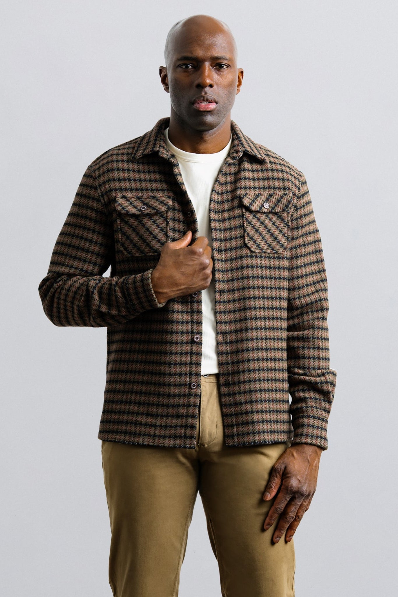 Man wearing a plaid shirt over a white t-shirt with beige pants on a light gray background