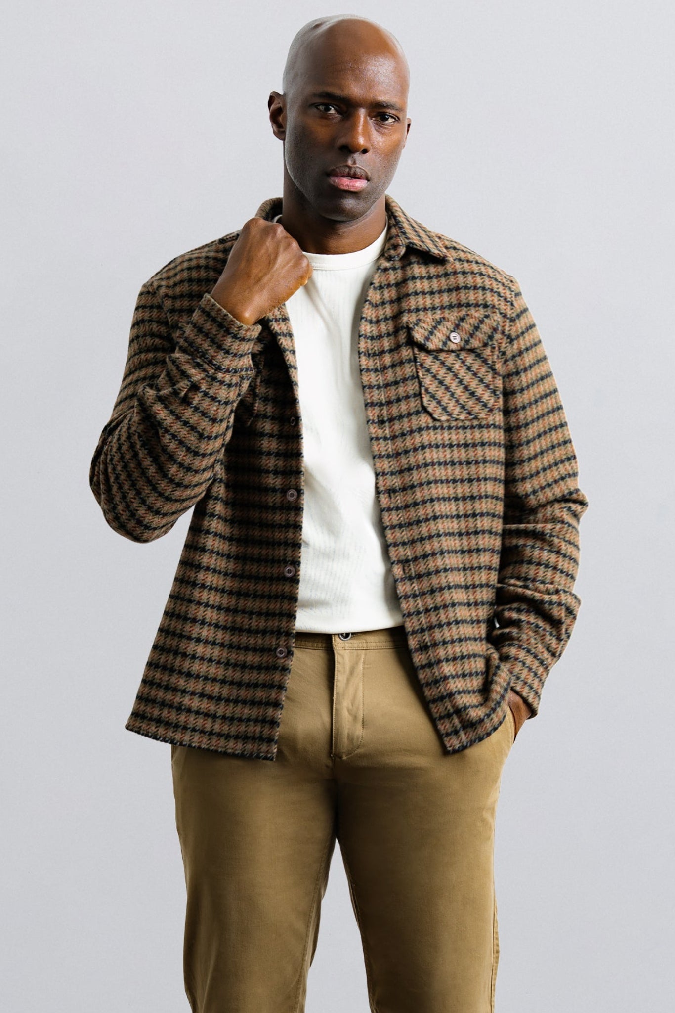 Man wearing a plaid jacket over a white shirt and beige pants on a light gray background
