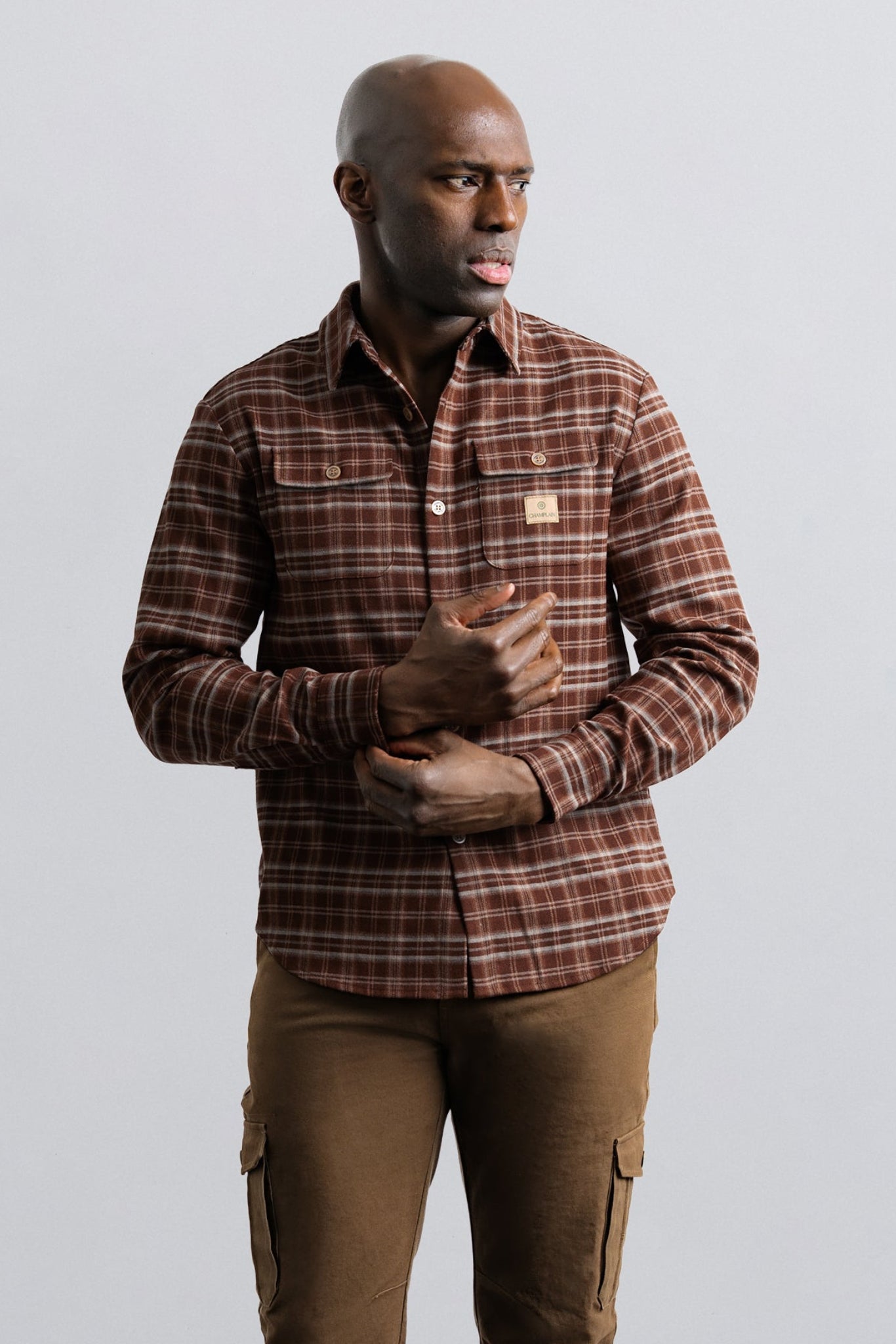 Man wearing a brown plaid shirt and brown pants against a plain background