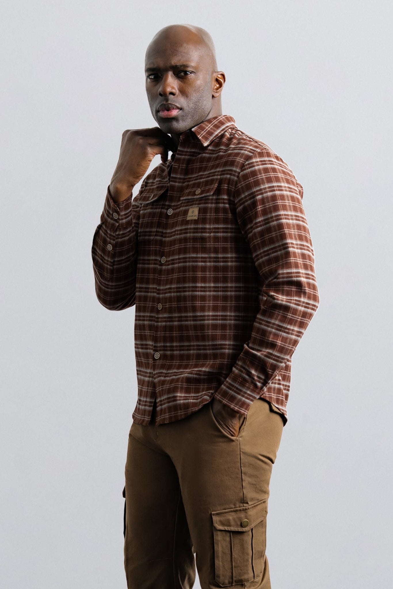 Man wearing a plaid shirt and brown pants against a plain background