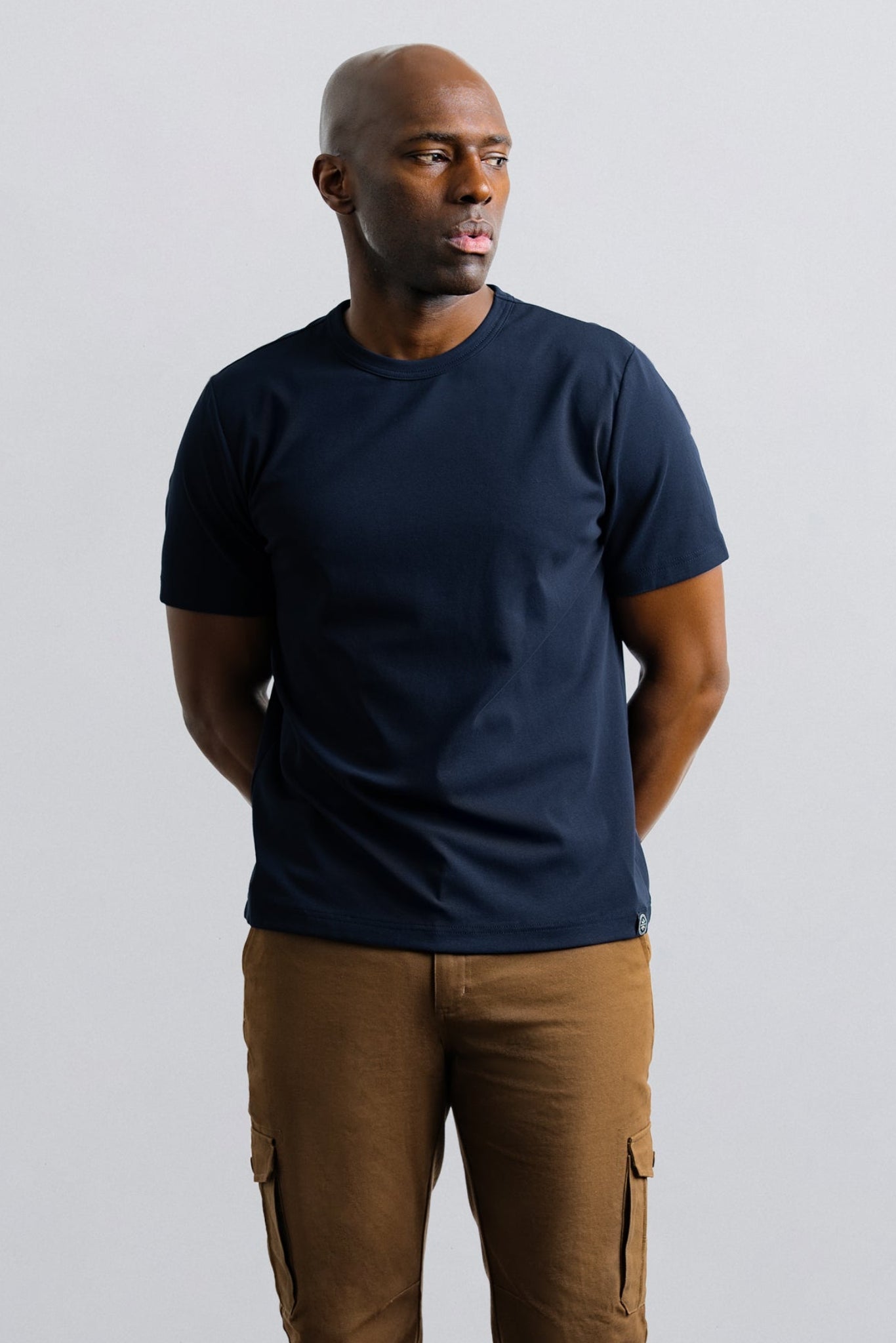Man wearing a navy t-shirt and brown pants against a plain background