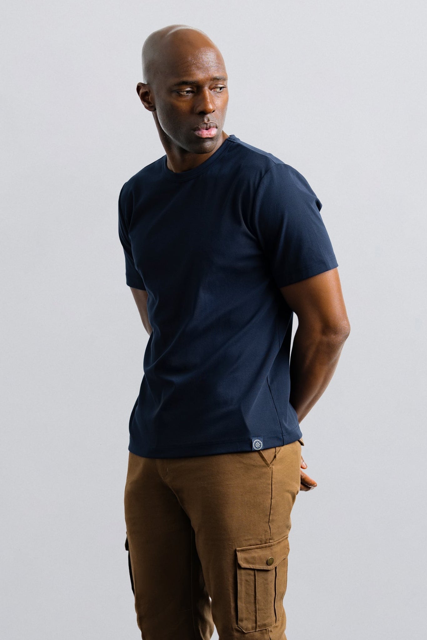 Man wearing a navy t-shirt and brown cargo pants against a plain background