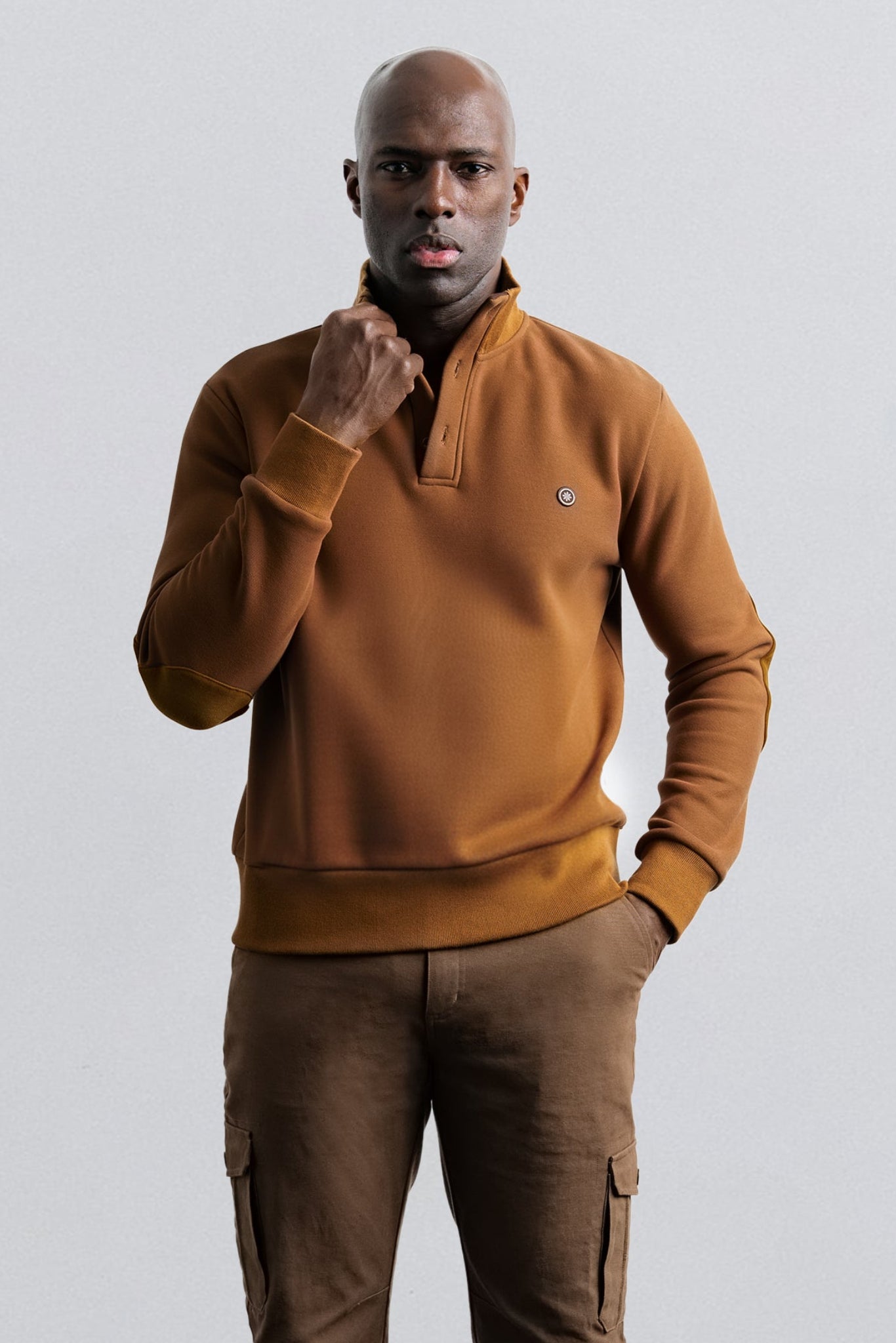 Man wearing a brown pullover and pants against a light gray background