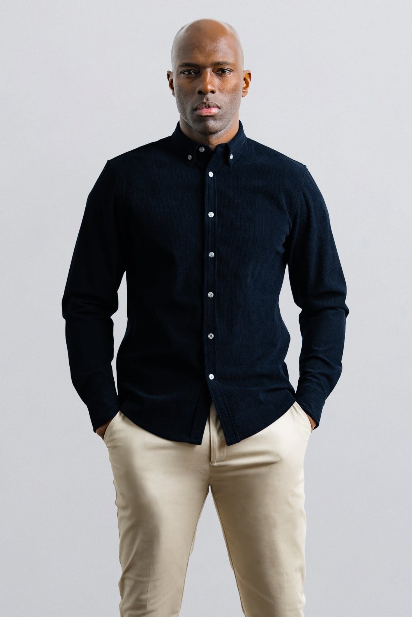 Man wearing a black shirt and beige pants against a light gray background