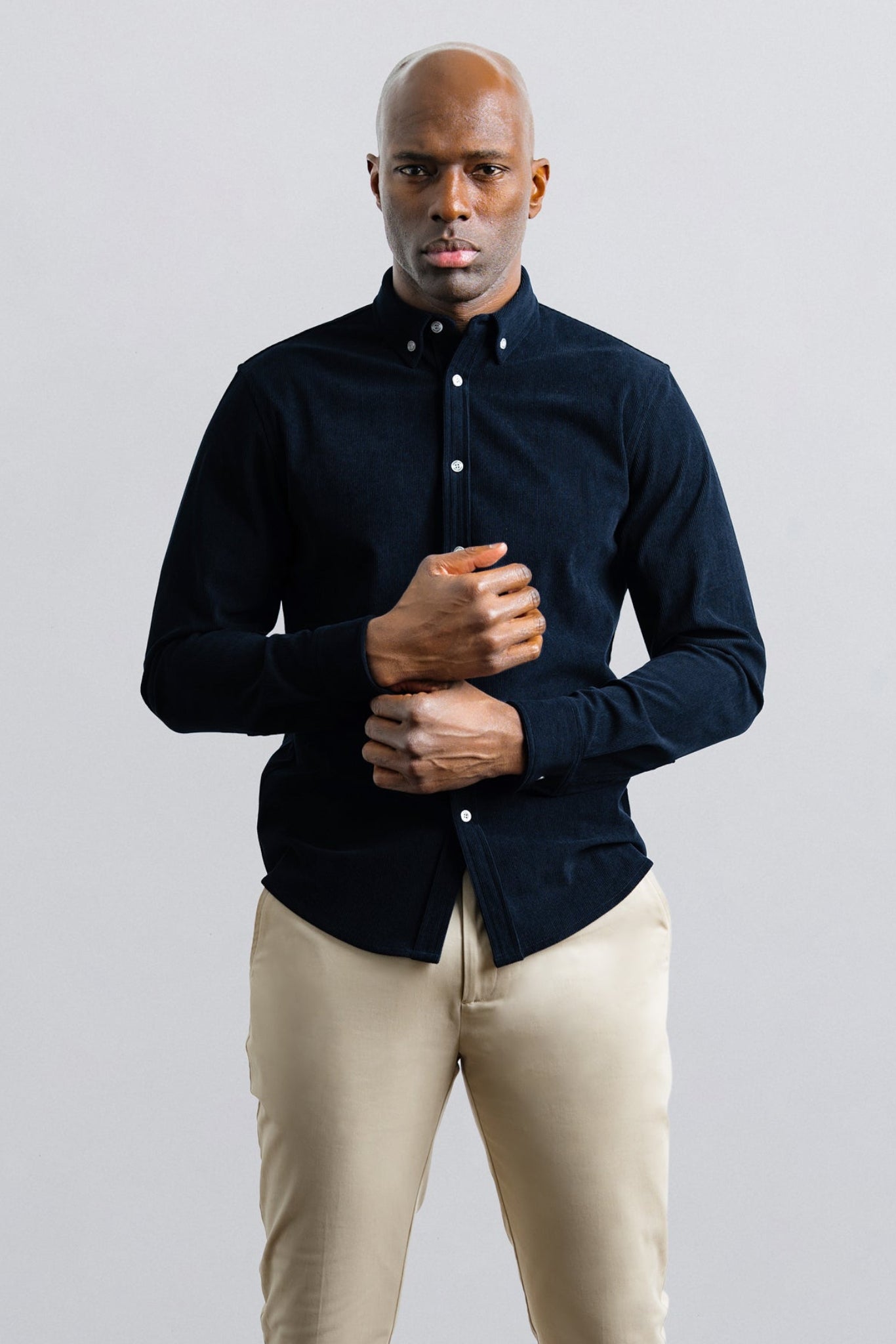 Man wearing a dark blue shirt and beige pants against a light gray background