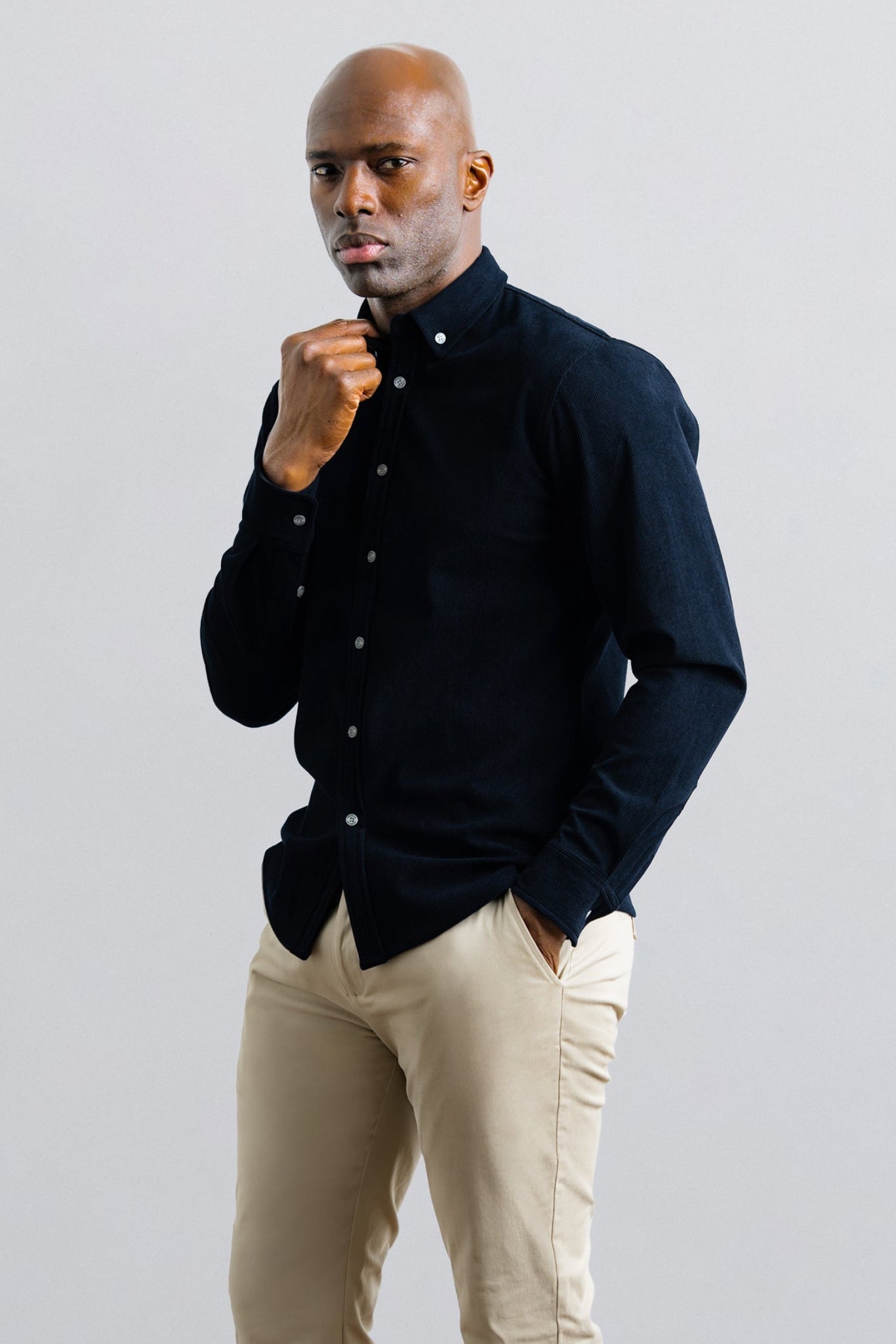 Man wearing a dark sweater and beige pants against a light gray background