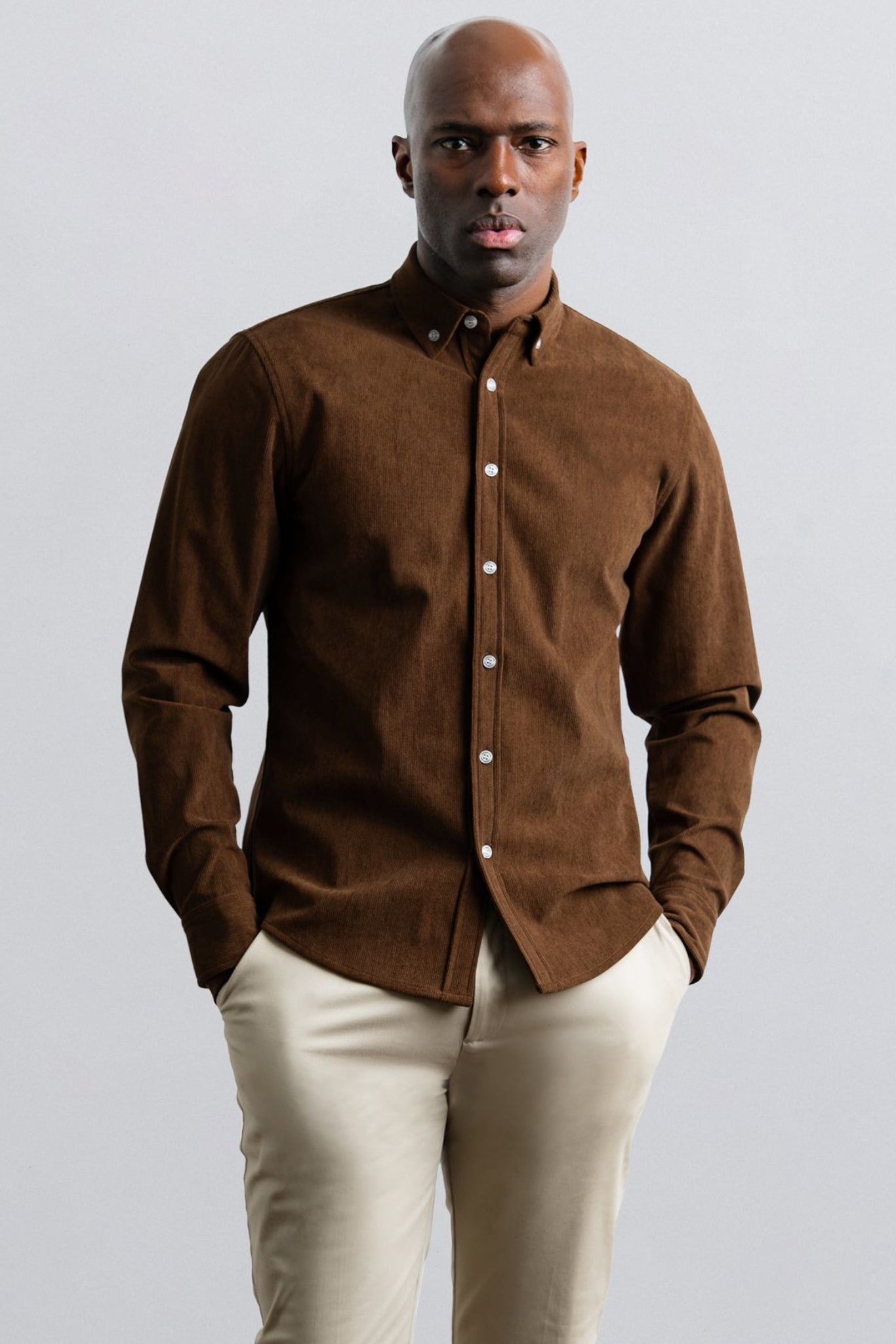 Man wearing a brown shirt and beige pants against a light gray background