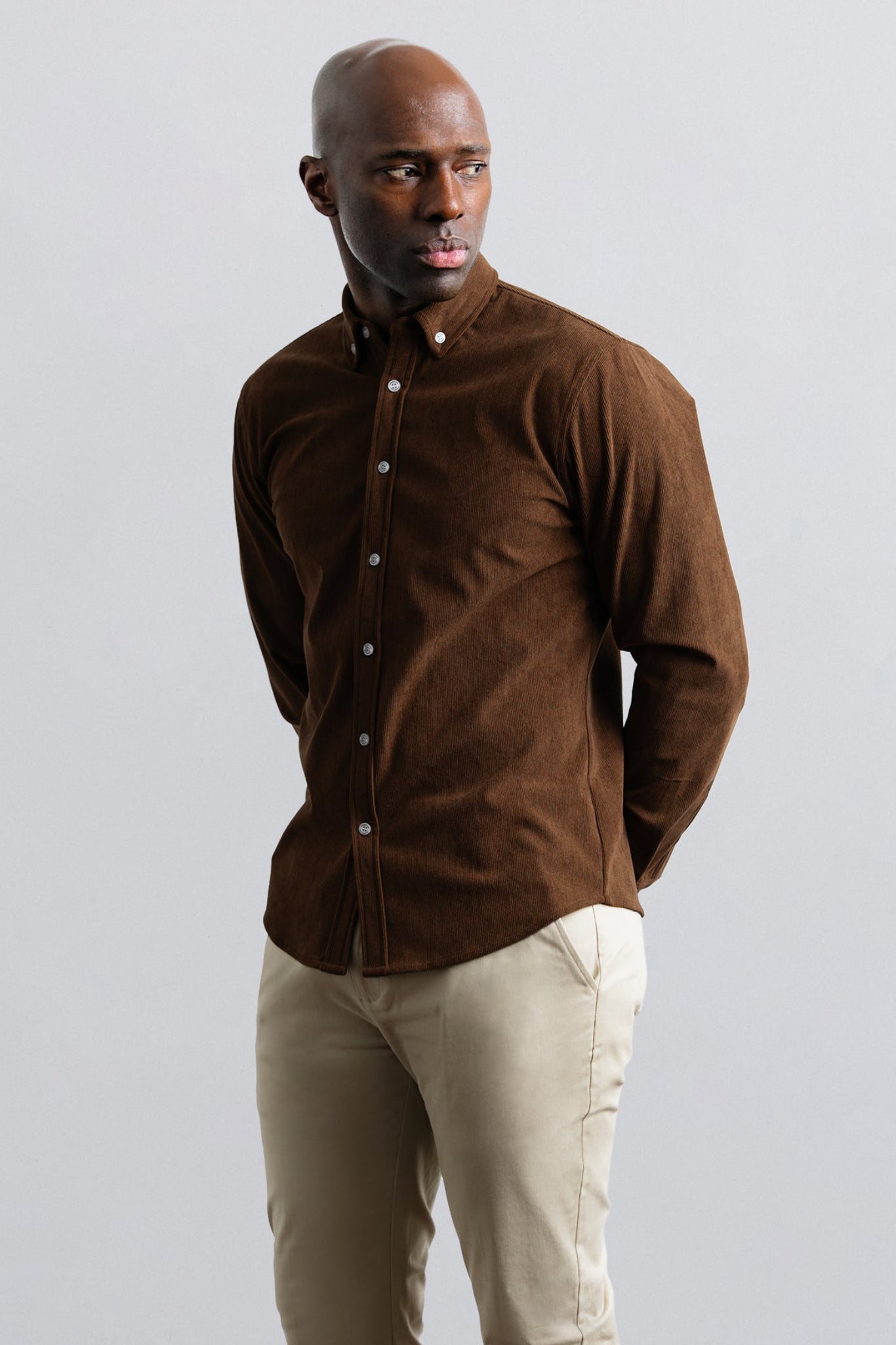 Man wearing a brown shirt and beige pants against a plain background