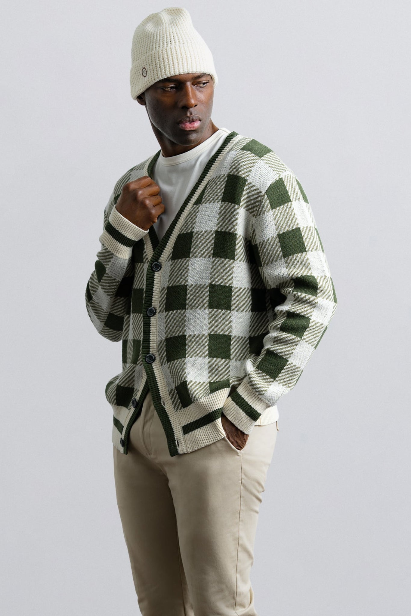 Person wearing a green and white checkered cardigan with beige pants and a white beanie on a light gray background