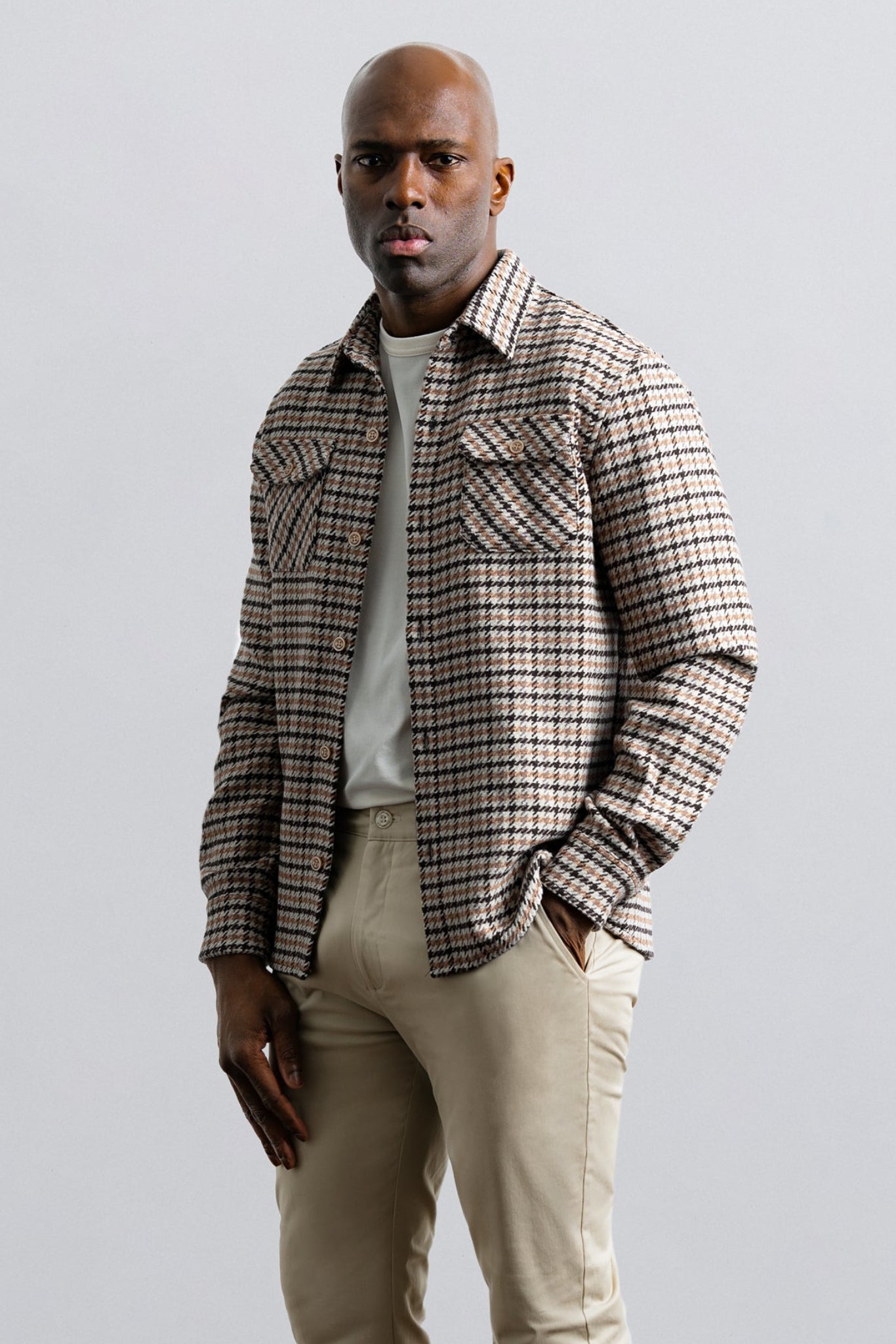Man wearing a plaid shirt over a white t-shirt with beige pants on a light gray background