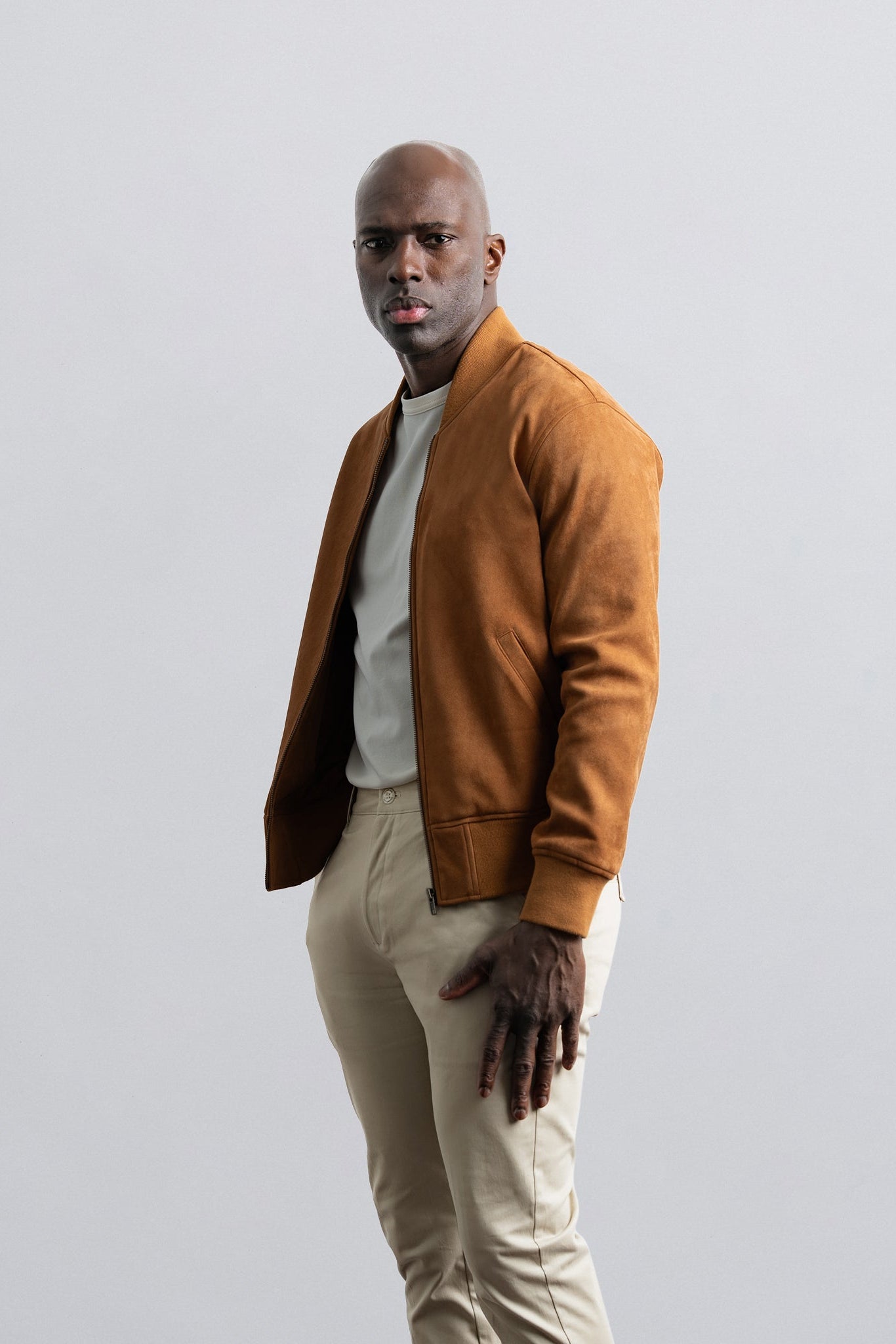 Man wearing a brown jacket and beige pants against a plain background