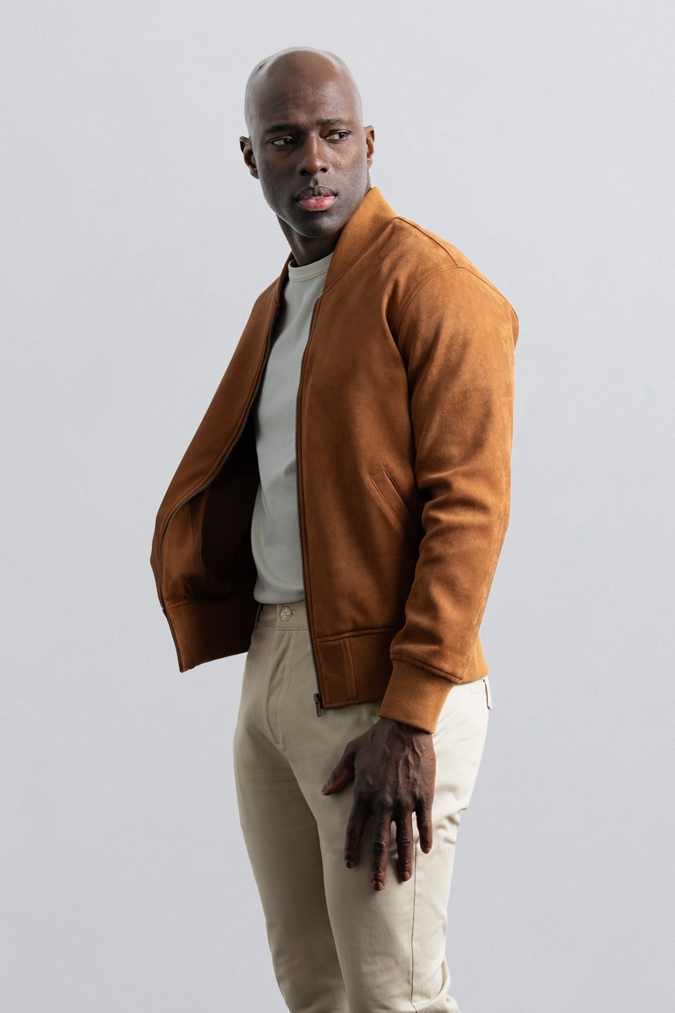 Man wearing a brown jacket and beige pants against a light gray background